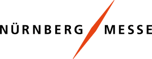 Logo der NürnbergMesse mit dem Schriftzug „NÜRNBERG MESSE“ in Schwarz, getrennt durch einen orangefarbenen stilisierten Schrägstrich. Der Hintergrund ist weiß.