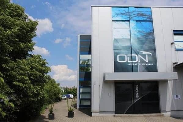 Modernes Bürogebäude mit Glasfassade trägt das Logo „ODN Internet Systemhaus“. Der mit „Eingang“ gekennzeichnete Eingang lässt auf eine sorgfältige Innenausbauweise schließen. Klarer Himmel und grüne Bäume lassen auf die Umgebung eines Gewerbeparks schließen.