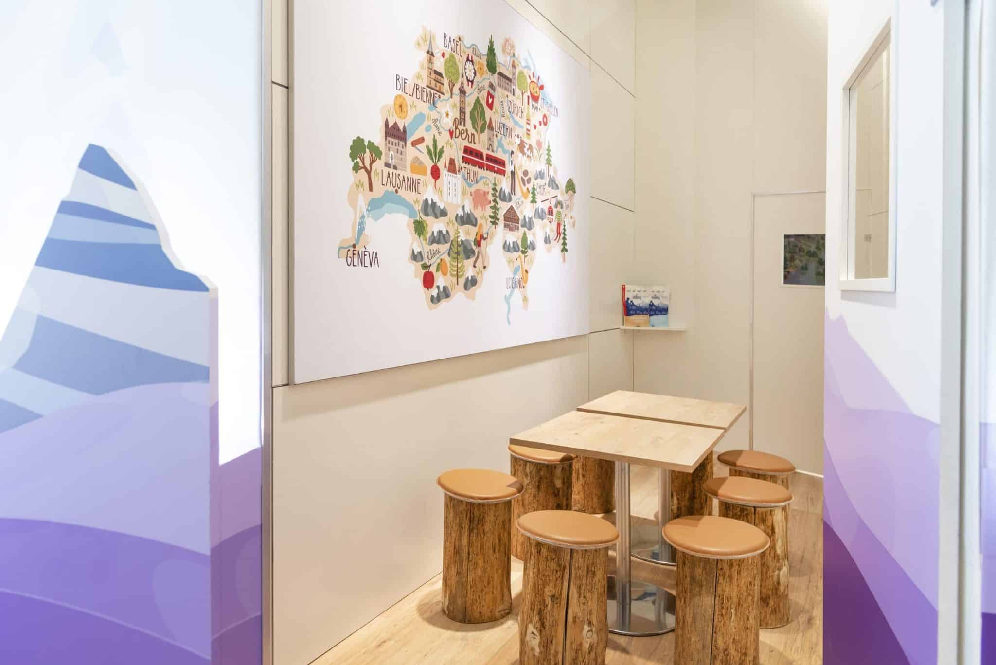 Messebau Nürnberg – Lounge-Bereich des Inzerzoo Stands mit Holztisch, Hockern und Wandgrafik.