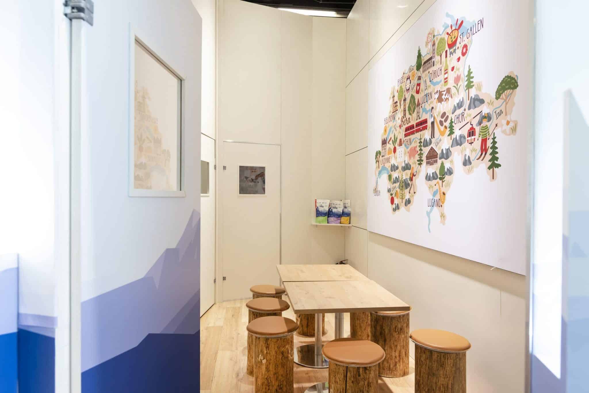 Messebau Nürnberg – Sitzbereich im Inzerzoo Messestand mit Holzhockern und Schweizer Landkarte.