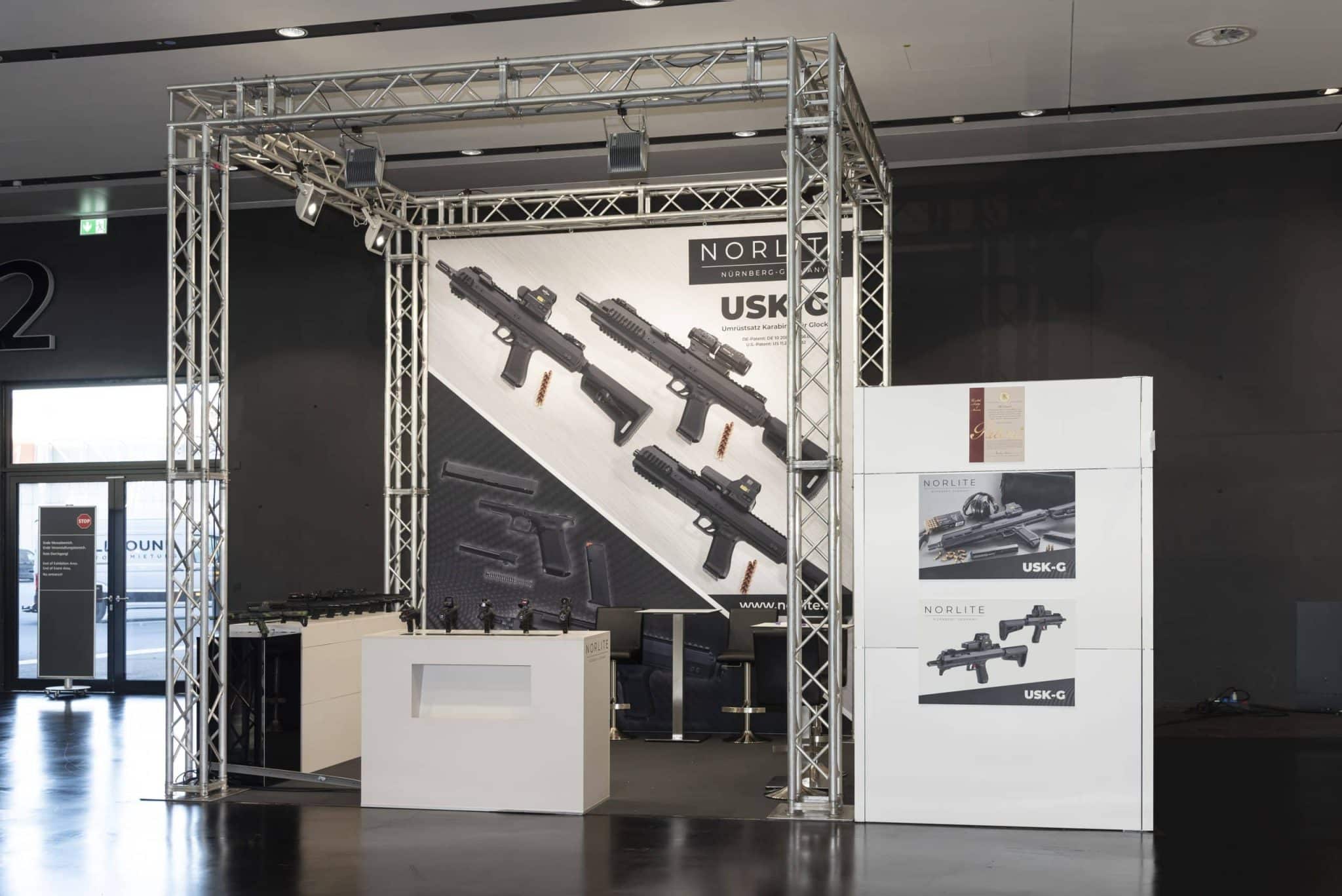 Vorderansicht des Norlite Messestands auf der IWA OutdoorClassics in Nürnberg mit ausgestellten USK-G Karabinern und großem Hintergrundbanner.