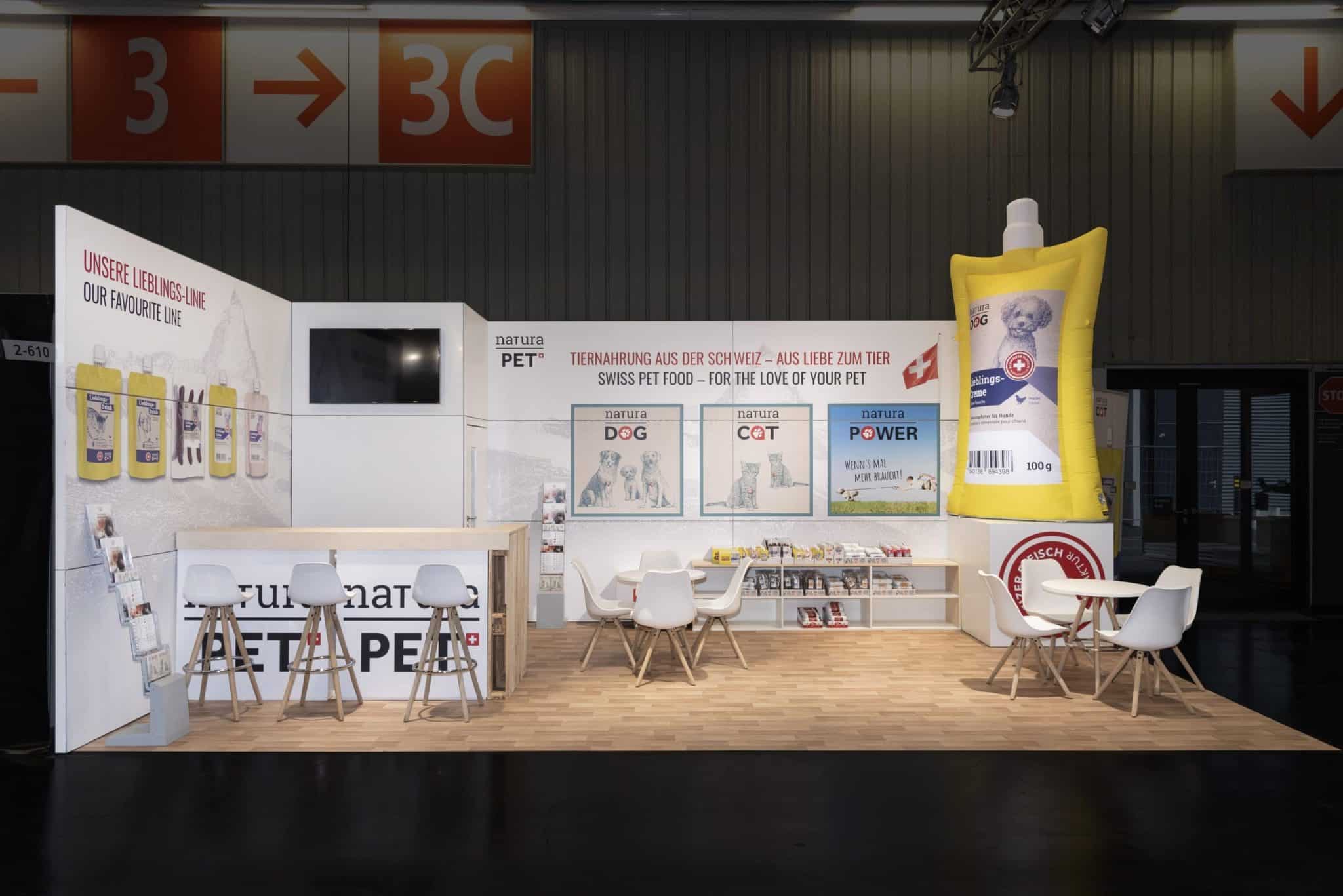 Gesamtansicht des NaturaPet Messestandes auf der Interzoo in Nürnberg mit Sitzbereich, Bar und großem Werbe-Display für Hunde- und Katzenfutter.
