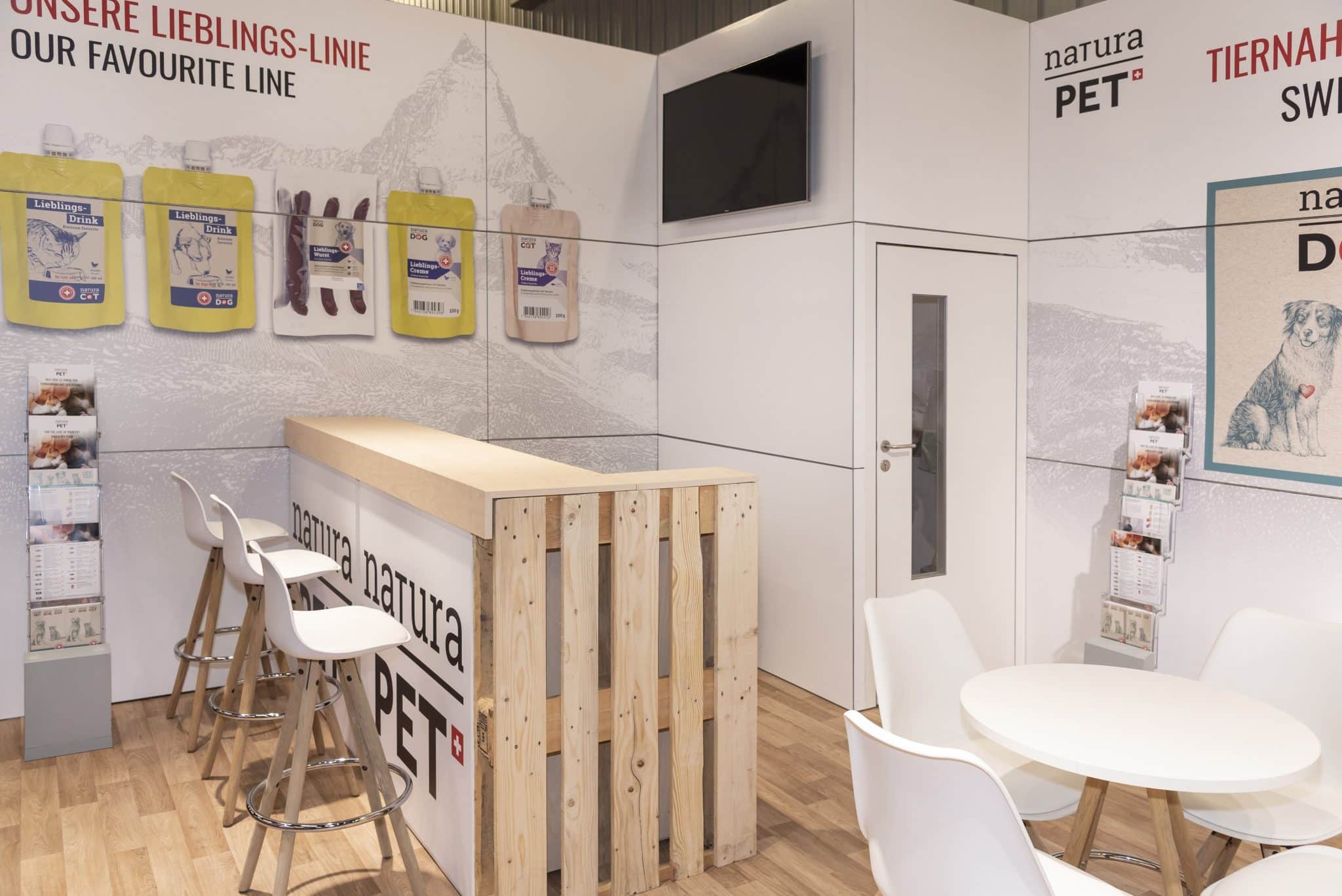 Moderner Messestand von NaturaPet auf der Interzoo in Nürnberg mit Bar, weißen Stühlen und Wandgrafiken für Hunde- und Katzennahrung.