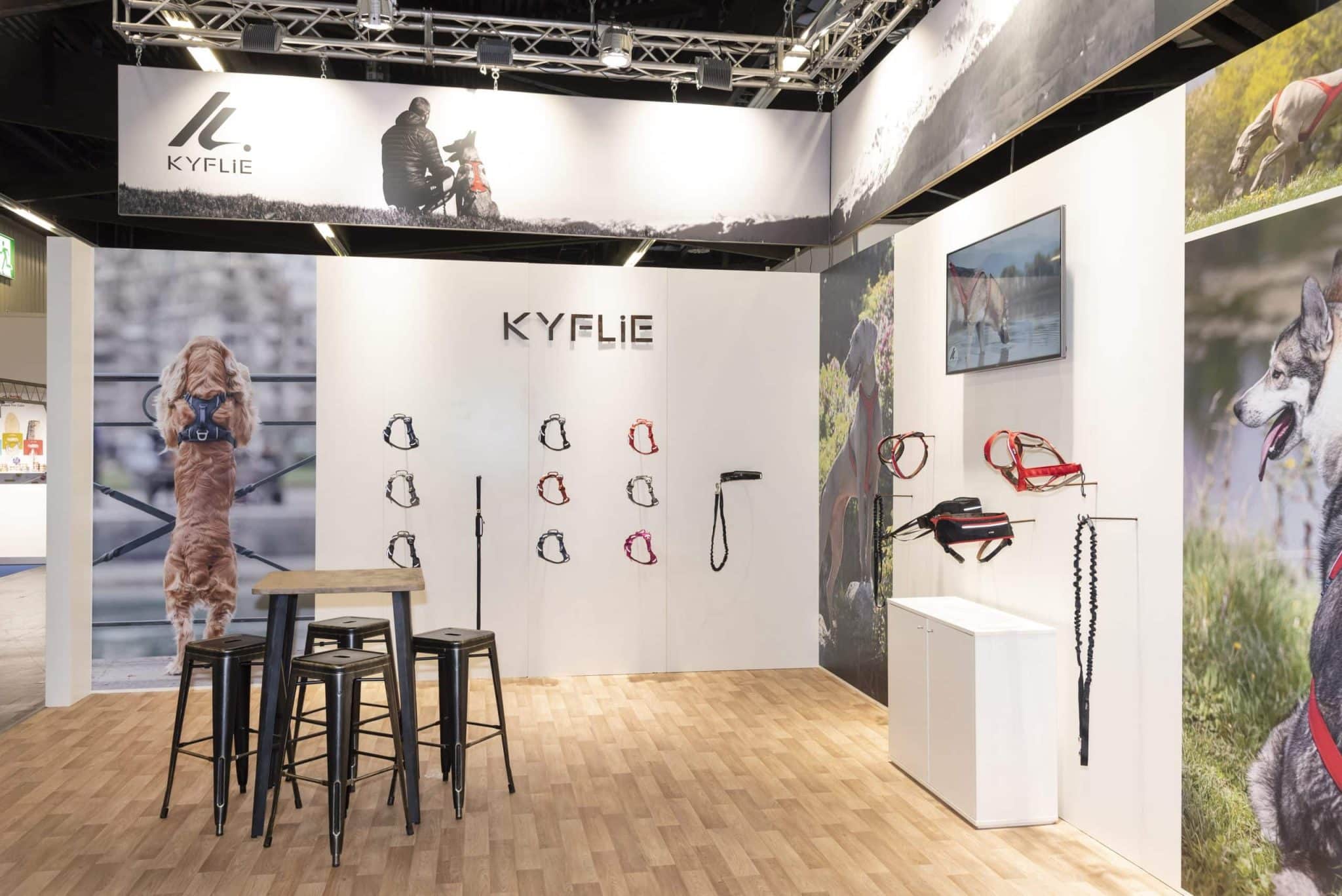 Präsentation der Kyflie Hundegeschirre und Leinen am Messestand auf der Interzoo Nürnberg, mit Produktwand, TV-Screen und Stehtisch mit Barhockern.