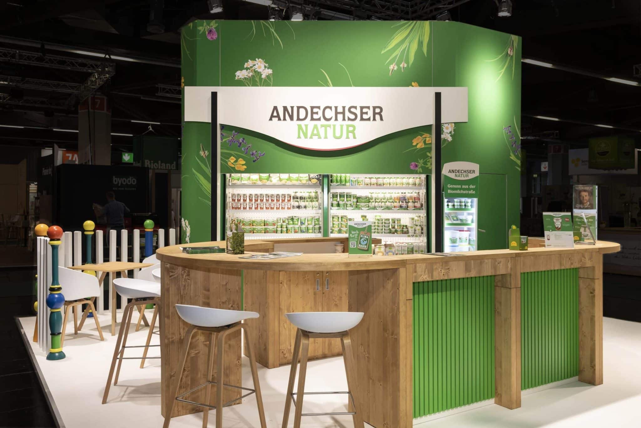 Moderner Messestand von Andechser Natur mit Holztheke und Kühlschrank auf der Biofach in Nürnberg – Messebau Nürnberg.
