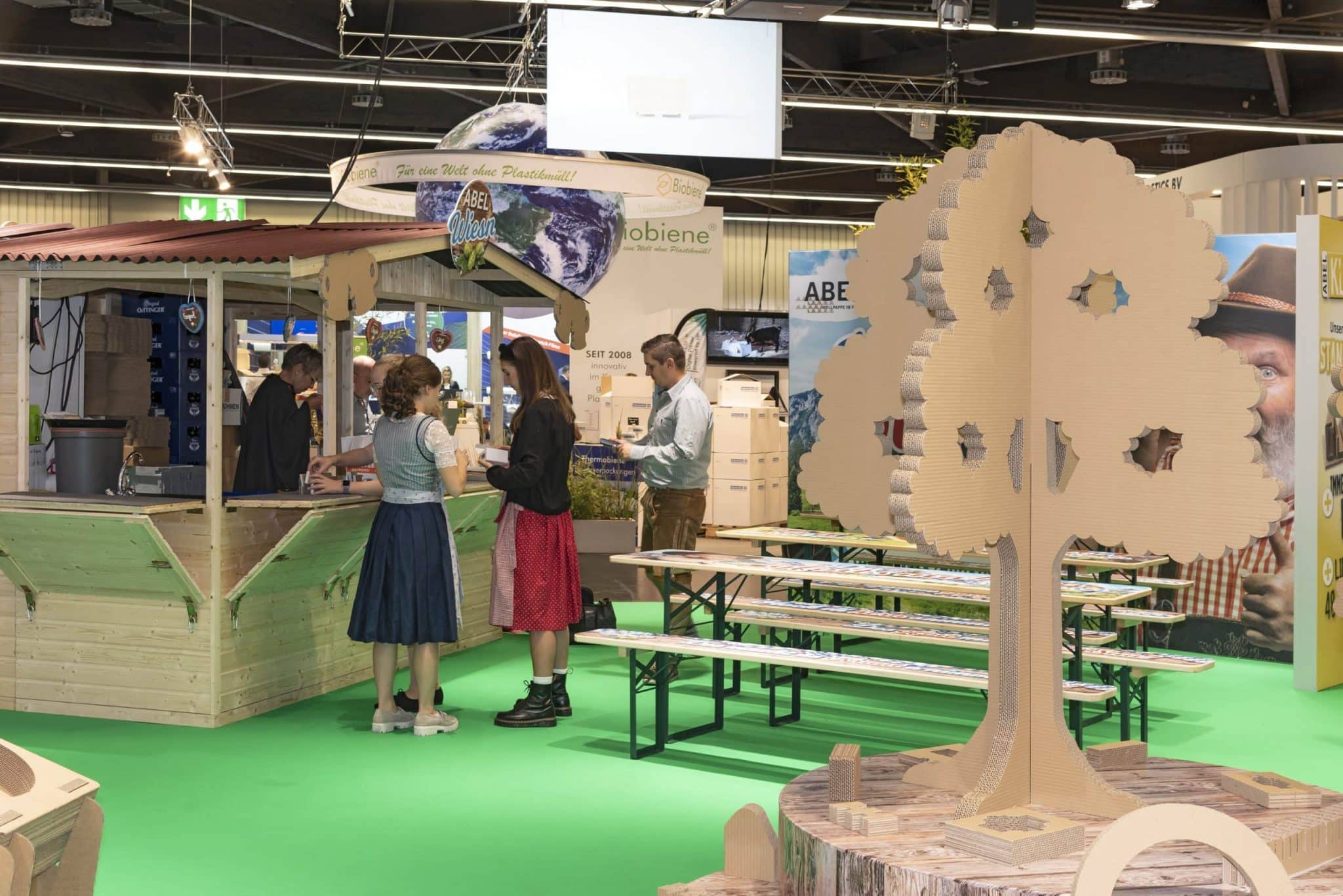 Besucher in Dirndl und Tracht am Abel Wiesn Messestand mit Holzhütte und Biertischen auf der Fachpack Nürnberg – Messebau Nürnberg.