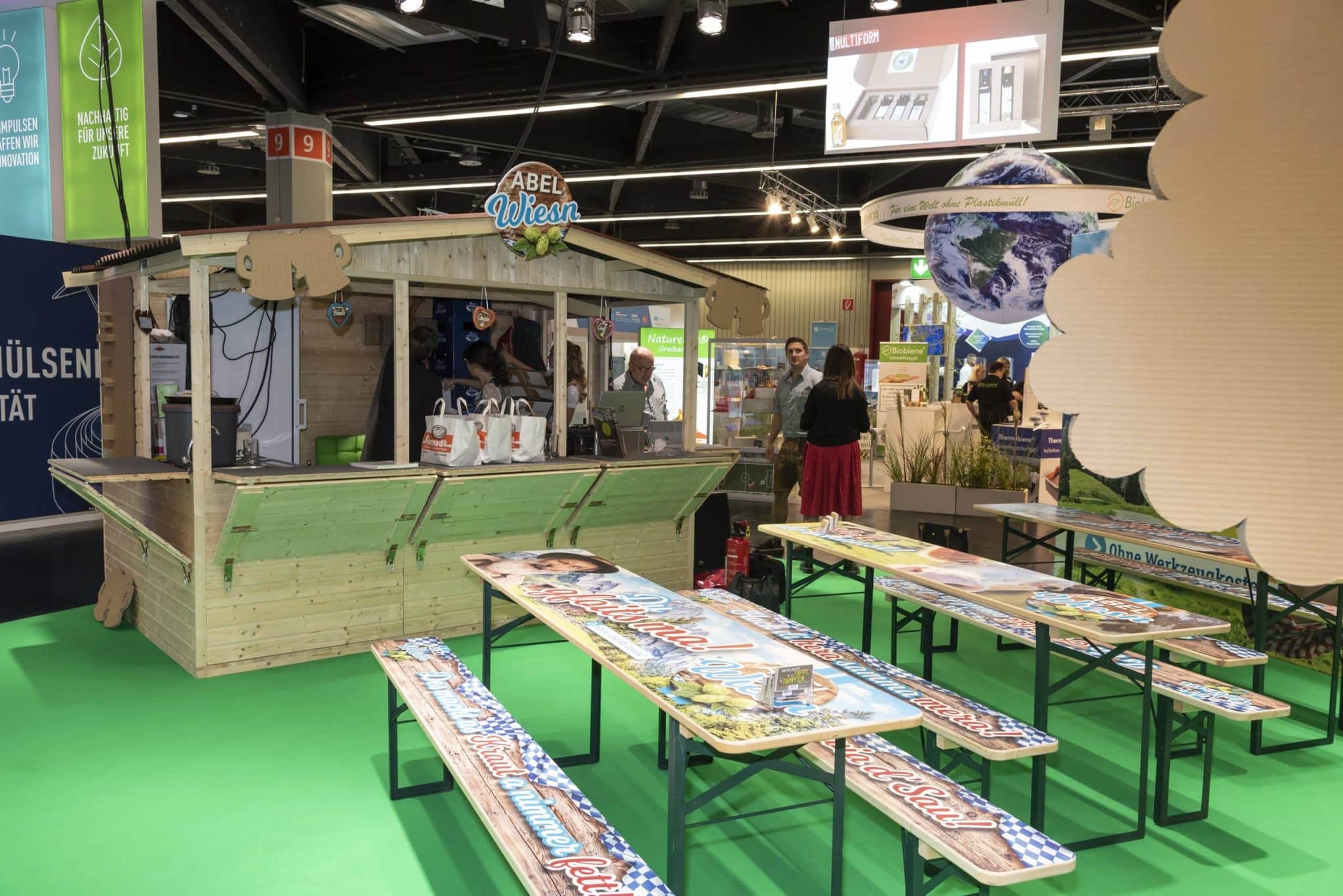 Traditioneller Messestand von Abel Wiesn auf der Fachpack Nürnberg mit bayerischer Holzhütte und dekorierten Biertischgarnituren – Messebau Nürnberg.