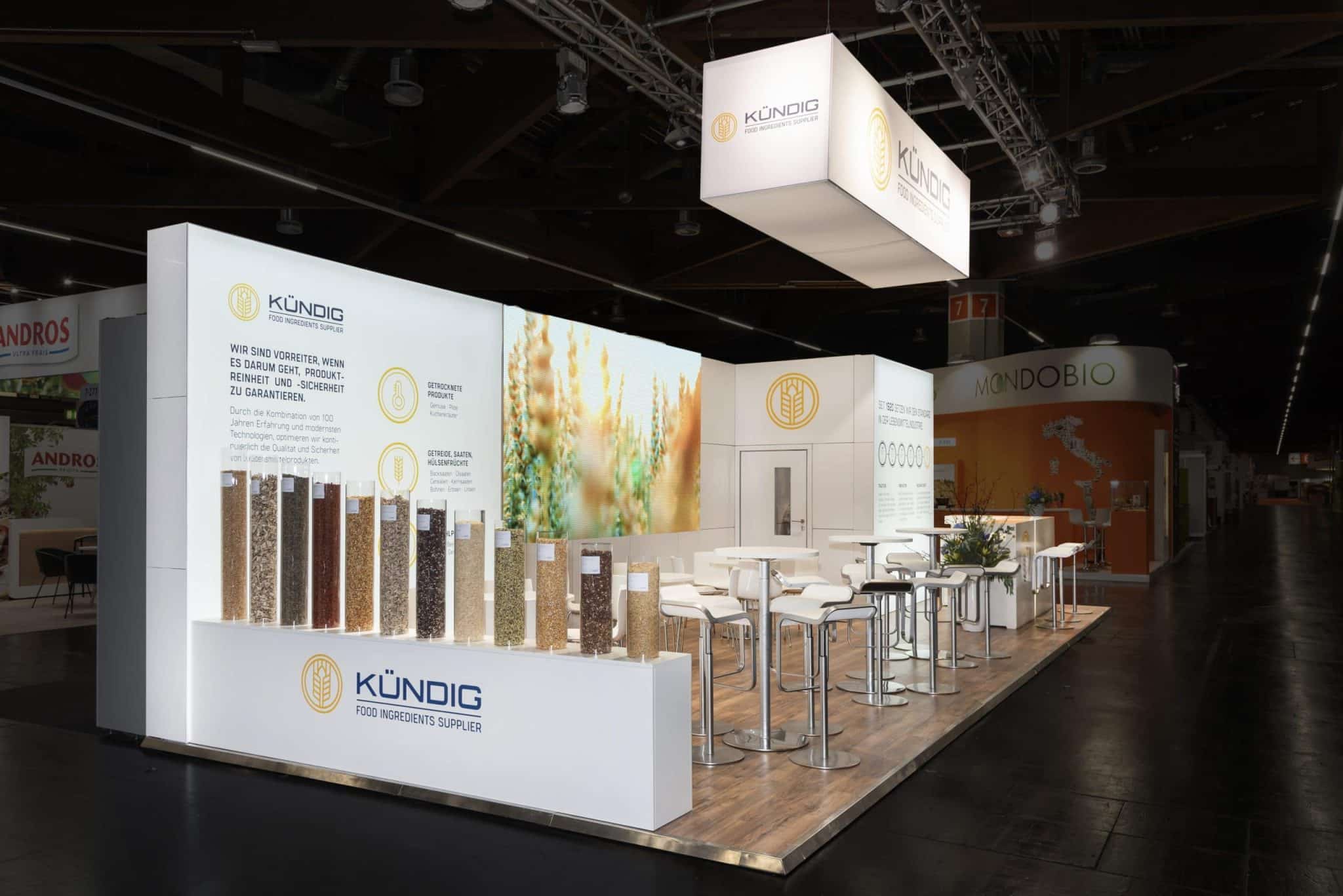 Messebau für Kündig auf der Biofach 2025 in Nürnberg mit Glasröhren voller Getreideproben und stilvoller weißer Einrichtung.
