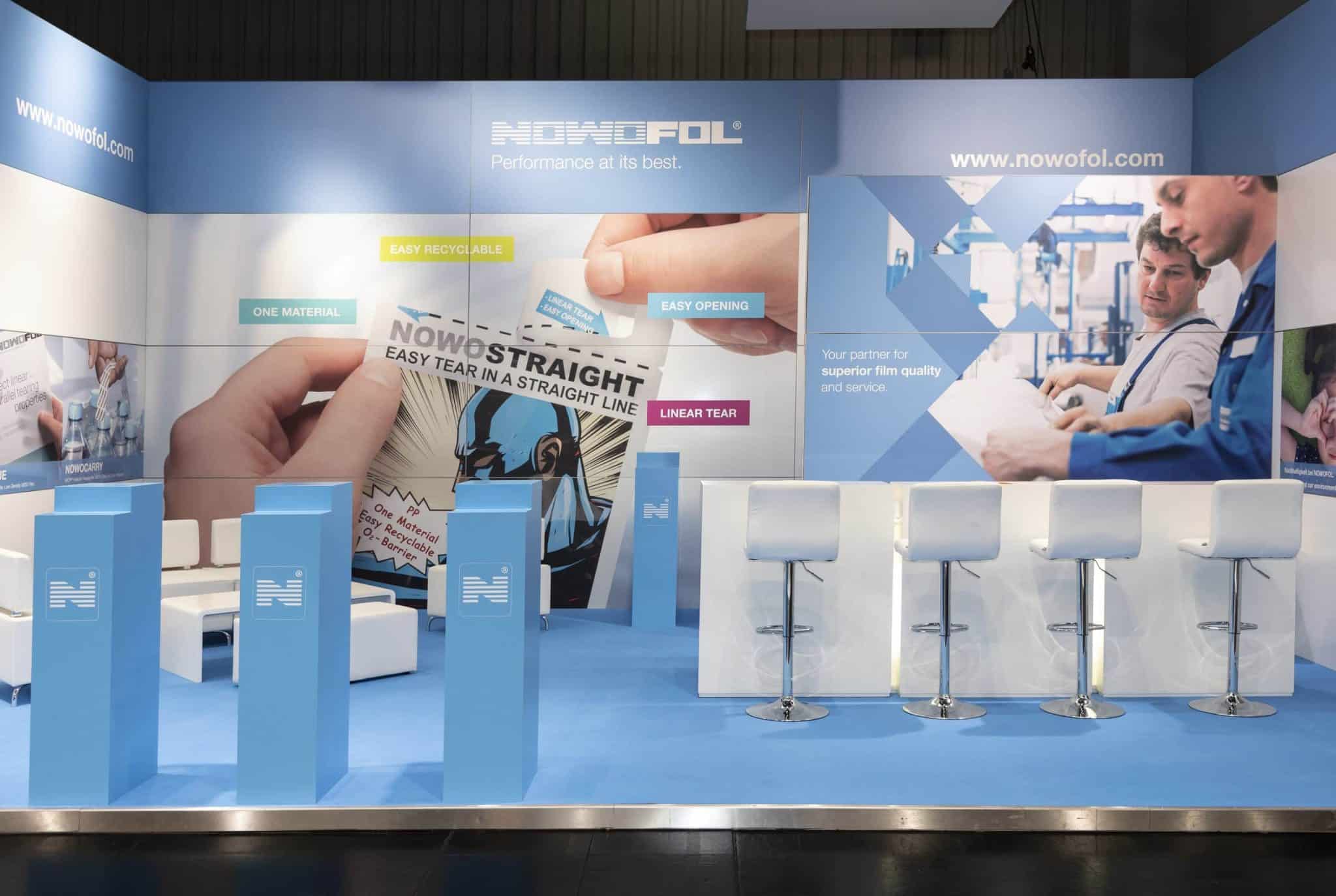Messestand von Nowofol mit weißen Barhockern und großflächigen Produktwänden auf der Fachpack in Nürnberg „Messebau Nürnberg“.