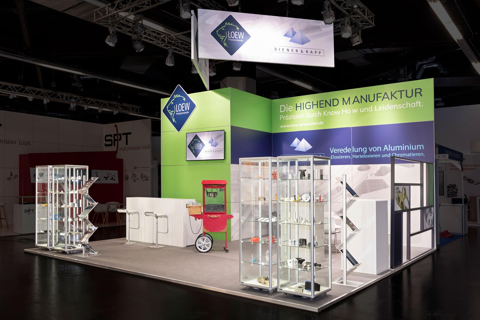Löew Präzisionsteile Messestand auf der Medtech Live 2023 mit Vitrinen voller Bauteile, Infotheke und auffälliger grüner Wandgestaltung.