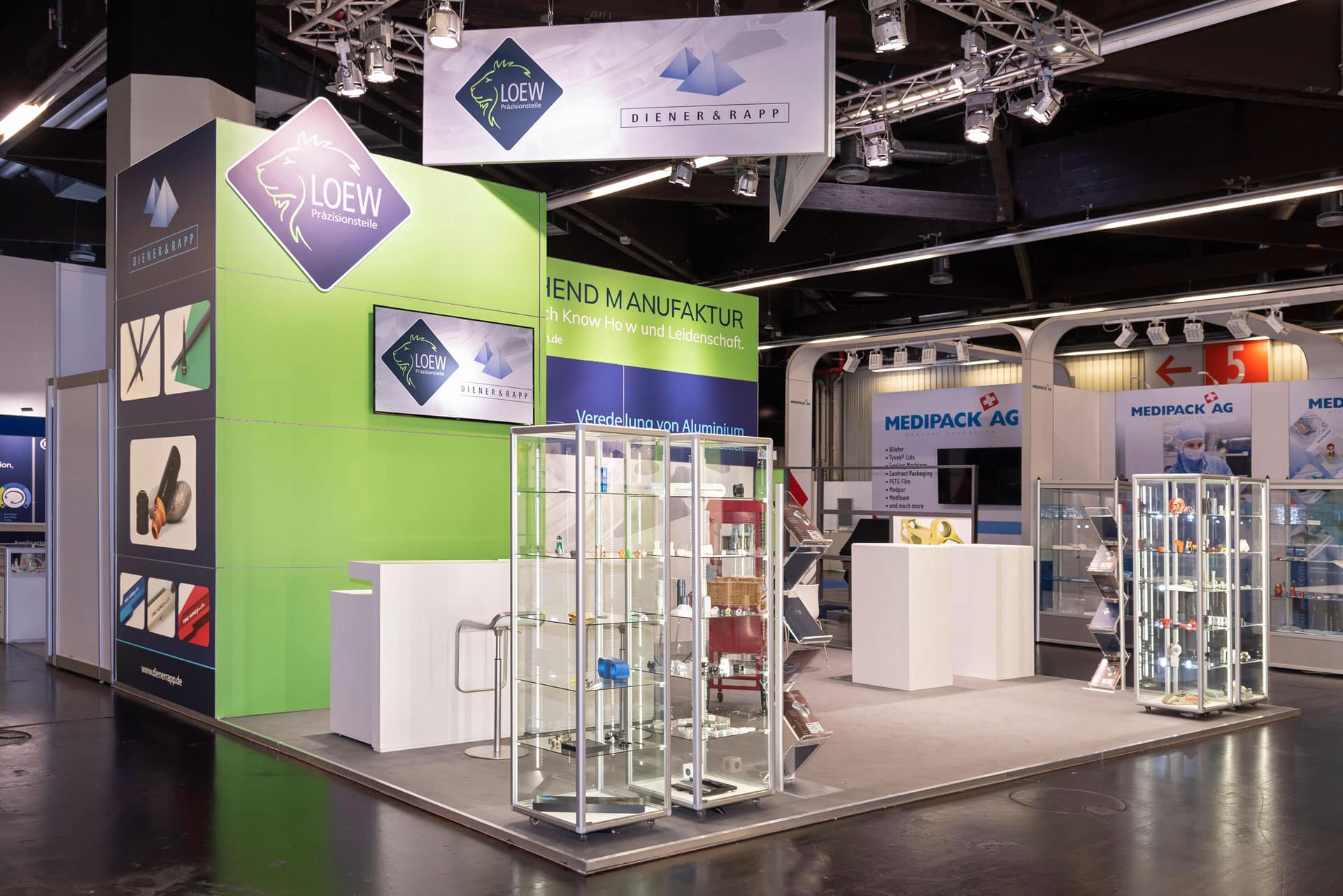 Messestand von Löew Präzisionsteile auf der Medtech Live 2023 mit Glasvitrinen, beleuchtetem Logo und Präsentationsflächen für Aluminiumveredelung.