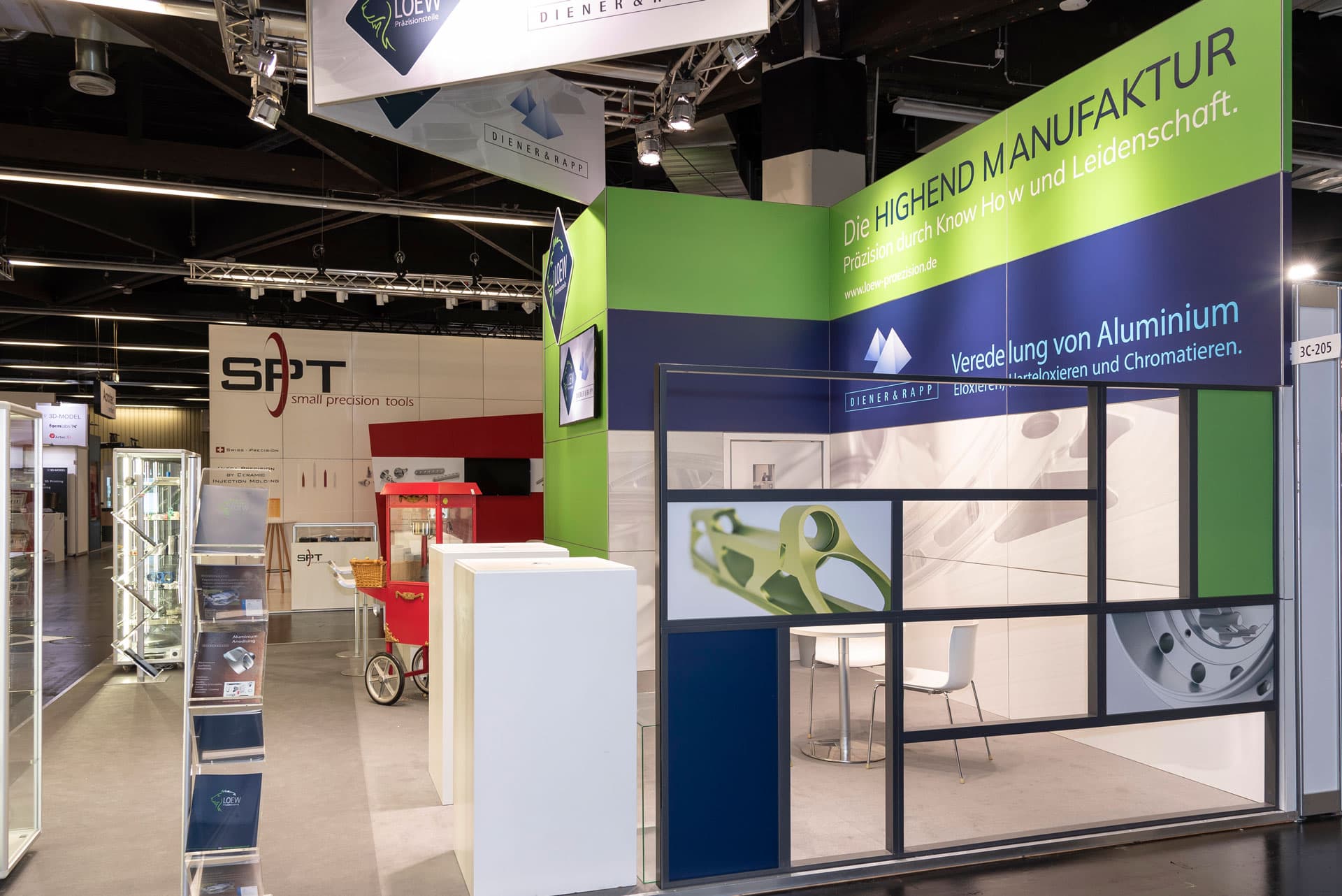 Messestand von Löew Präzisionsteile auf der Medtech Live 2023 in Nürnberg mit grün-blauem Design, Glasvitrinen und Aluminium-Bauteilen.