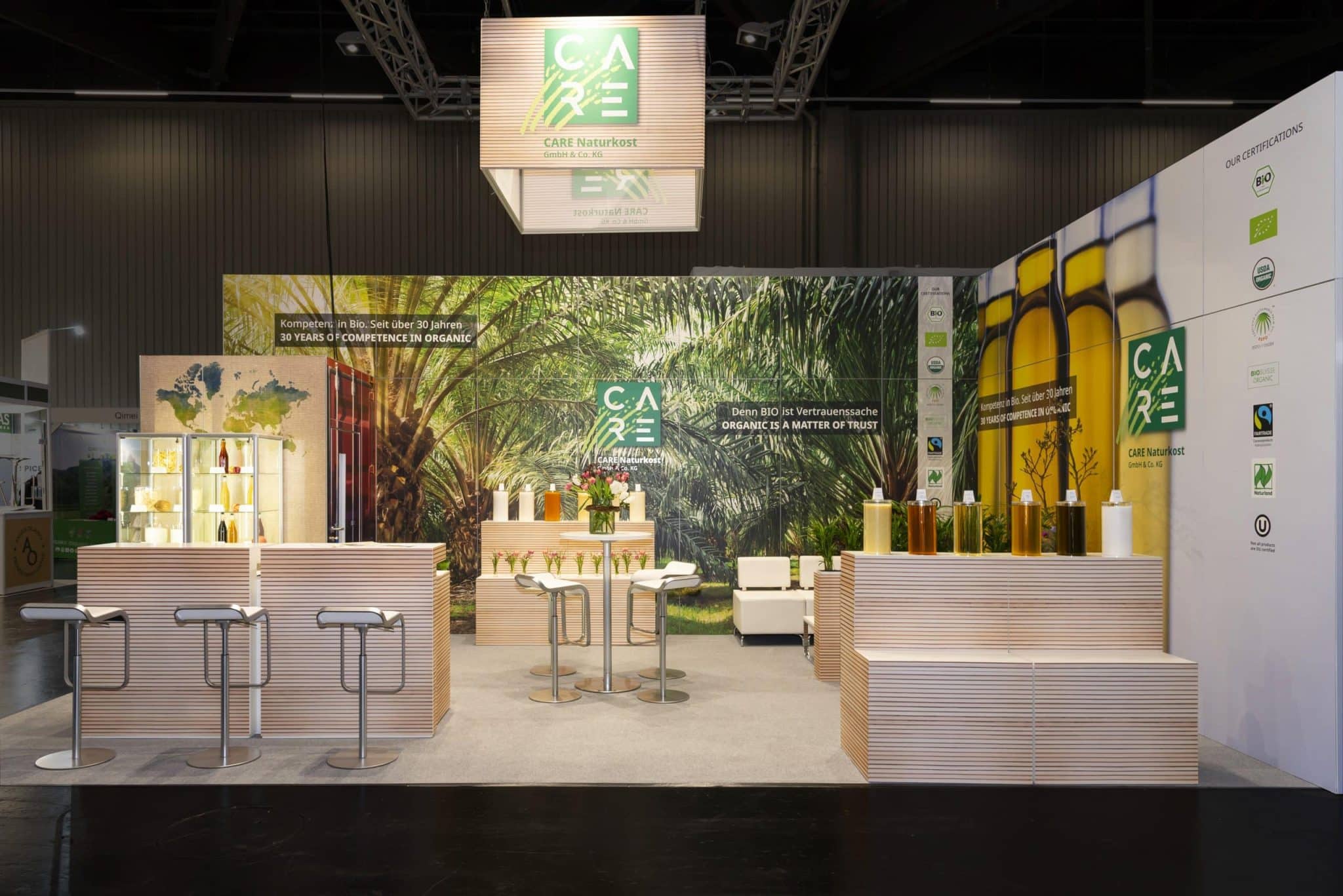 Eleganter Messestand von CARE Naturkost auf der BioFach Nürnberg mit Naturhintergrund und Theken – Messebau Nürnberg.