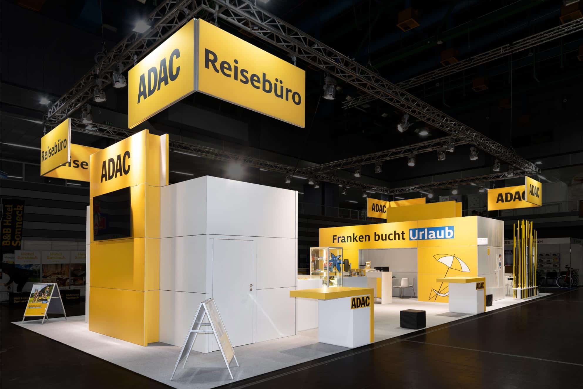 ADAC Reisebüro Messestand in Gelb-Weiß auf der Freizeitmesse 2024 in Nürnberg mit Slogan „Franken bucht Urlaub“.