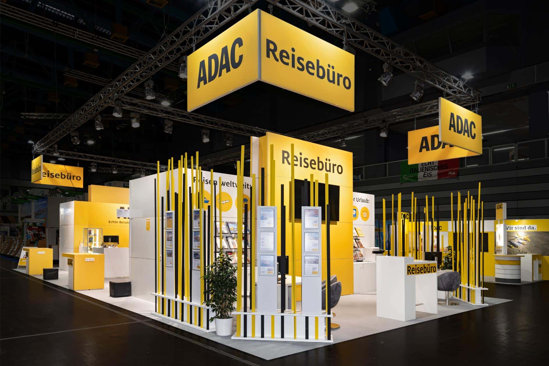 Moderner ADAC Messestand auf der Freizeitmesse 2024 in Nürnberg mit Reisebüro-Bereich, gelben Wandelementen und Infostelen.