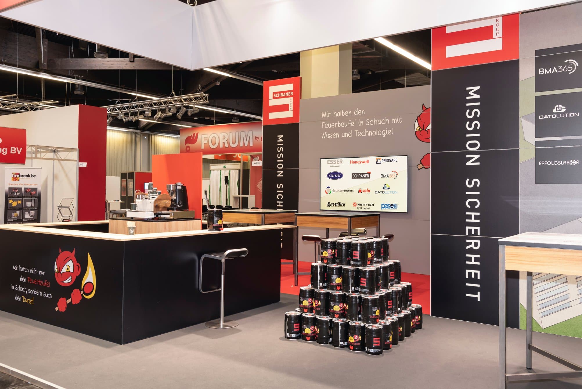 Präsentationsstand von Schraner Group auf der FeuerTrutz in Nürnberg mit Logo-Wänden und Getränkefässern.