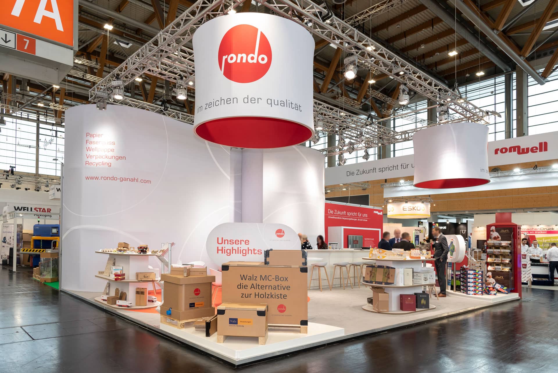 Der fachmännisch mit Messebau-Techniken errichtete Messestand präsentiert die Marke Rondo. Er präsentiert Werbematerialien, Kartons und Regale mit verschiedenen Produkten unter großen Bannern mit dem Rondo-Logo und regt die Besucher am Stand zum Austausch an.