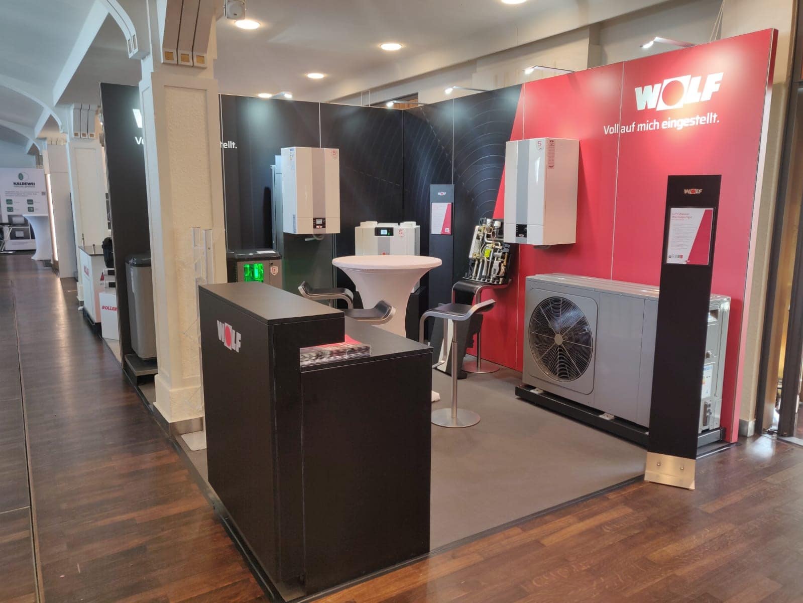 Messestand von WOLF auf der Sanitärmesse Ufer in Landau mit Wärmepumpen und Heizsystemen, modernem Design und roter Markenwand – Messebau Landau.