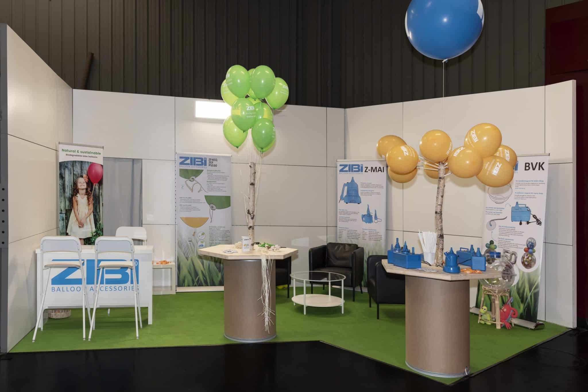 Messestand von ZIBI Balloon Accessories auf der Spielwarenmesse Nürnberg mit Ballonbäumen, Bannern zu ZIBI-Produkten und Sitzmöglichkeiten.