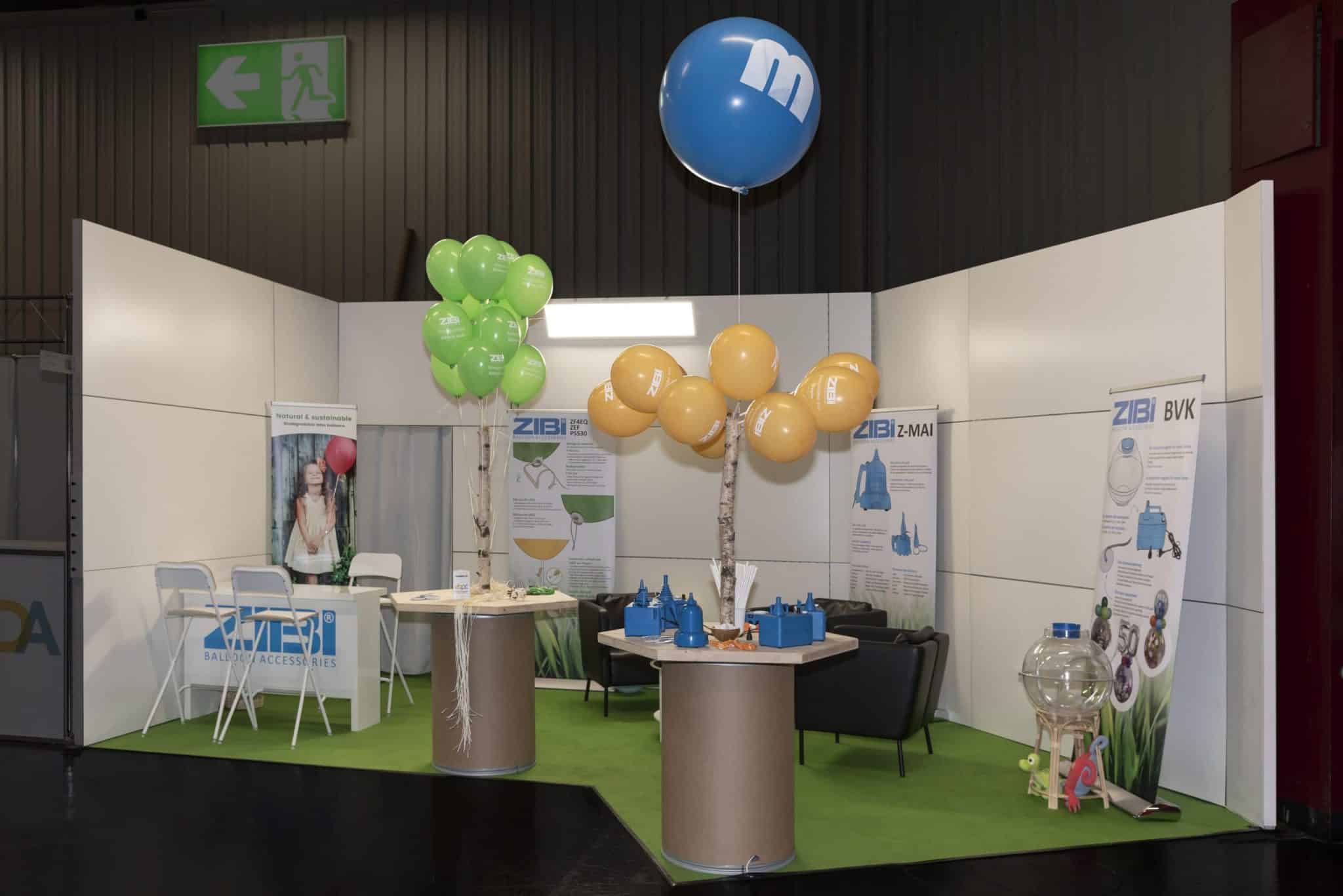 Messestand von ZIBI Balloon Accessories auf der Spielwarenmesse Nürnberg mit grünen, gelben und blauen Luftballons, Präsentationstischen und Bannern zu Ballonzubehör.