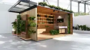 Eine moderne, offene Holzkonstruktion mit Pflanzen und Grünflächen auf dem Dach und an den Seiten. Dieser nachhaltige Messestand verfügt über Regale im Inneren und moderne Beleuchtung in einer geräumigen, hellen Umgebung und präsentiert sich in klarem, minimalistischem Design.