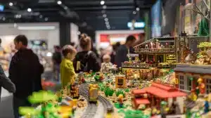 Auf der geschäftigen Spielwarenmesse Nürnberg bestaunen Besucher eine detailreiche LEGO City-Szene mit lebendigen Gebäuden, üppigem Grün und lebendigen Figuren. Diese detailreiche Ausstellung besticht durch ihre farbenfrohen und meisterhaft gefertigten LEGO-Strukturen.