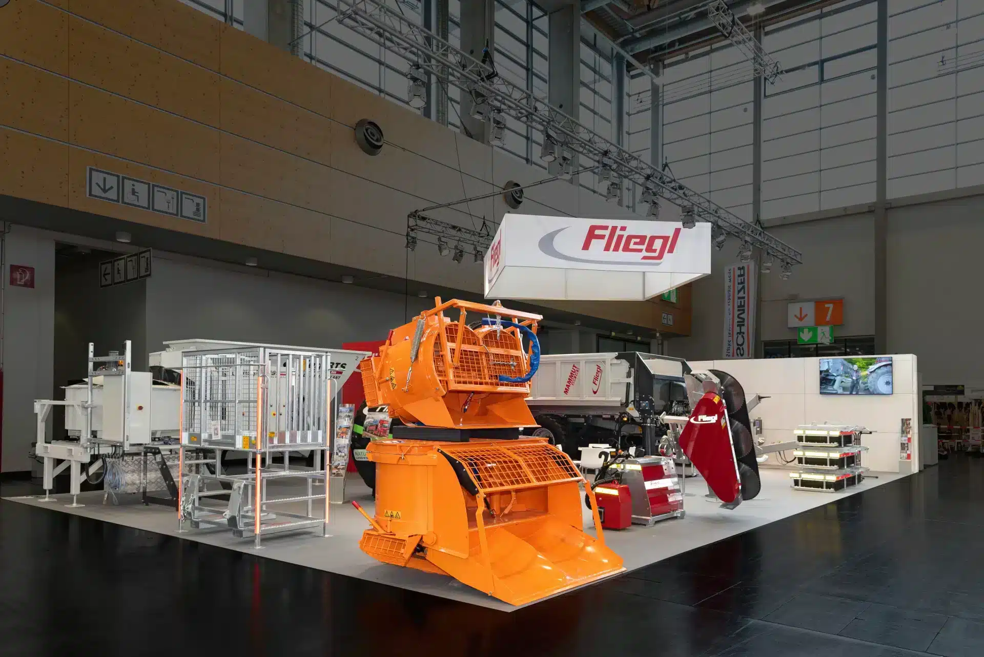 Moderner Messestand von Fliegl mit auffälliger orangefarbener Baumaschine auf der GaLaBau Nürnberg – Messebau Nürnberg.