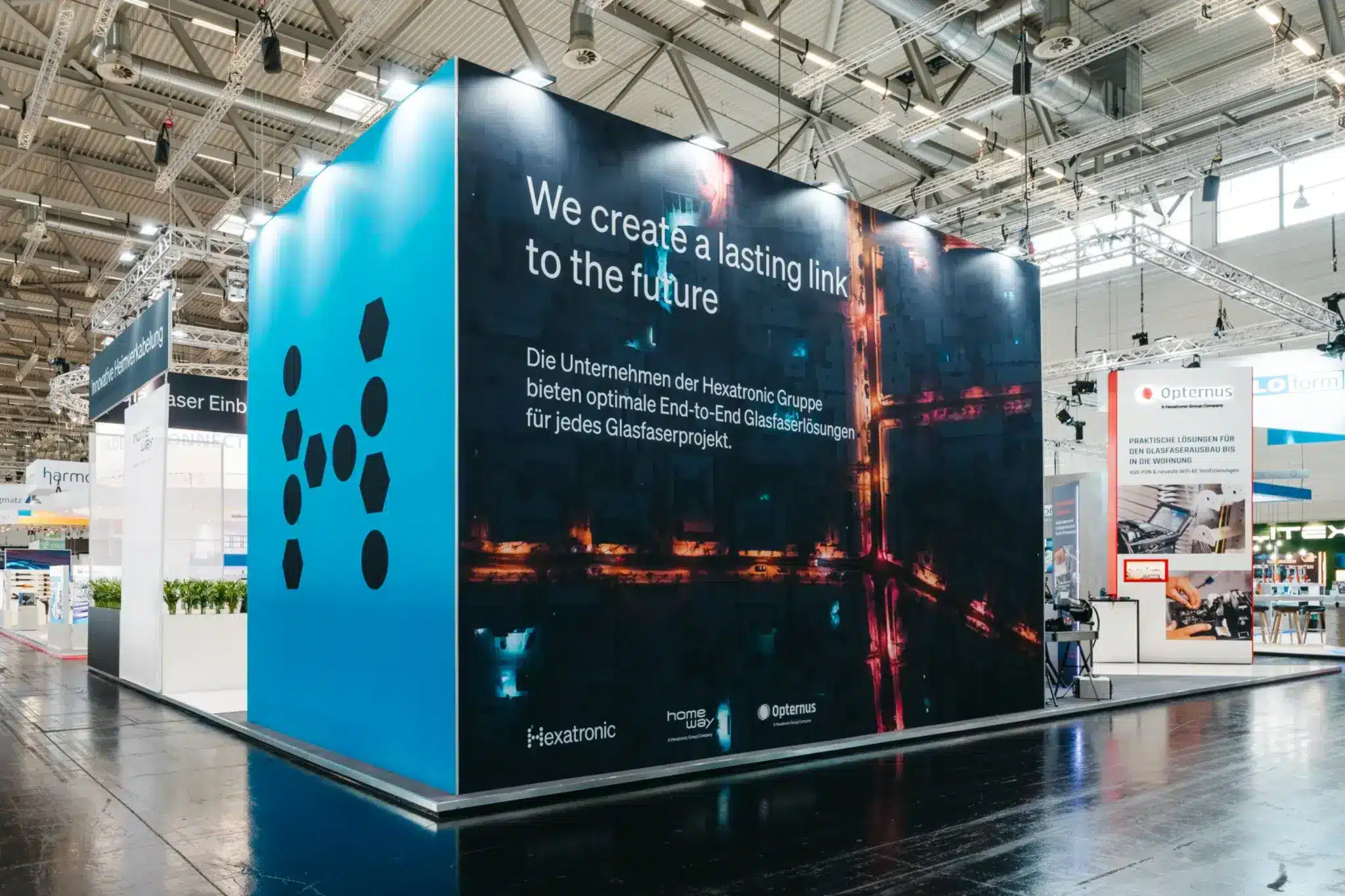 Großflächiger Banner am Hexatronic Messestand mit dem Slogan „We create a lasting link to the future“ auf der Köln Messe.