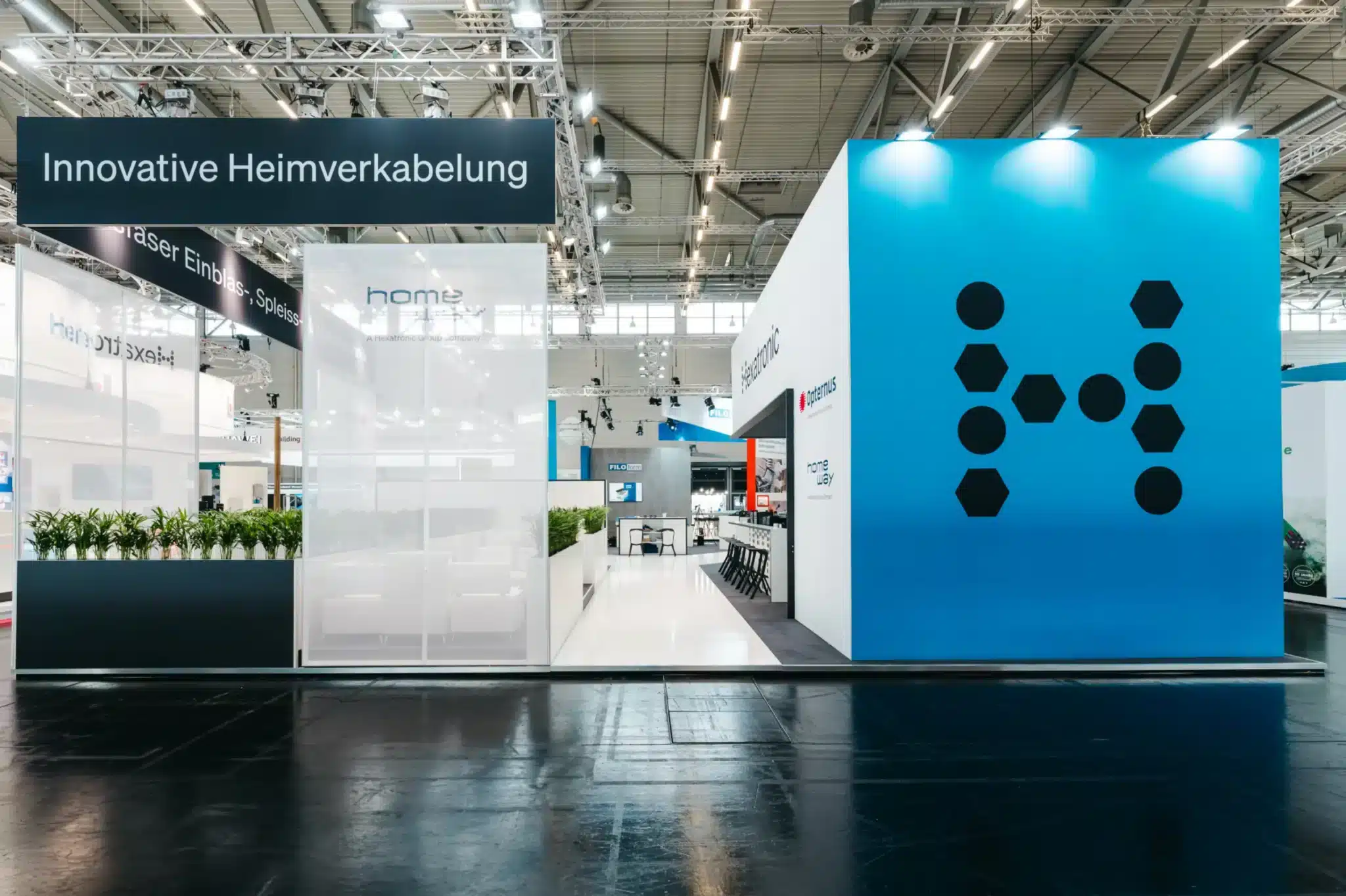 Seitenansicht des Hexatronic Messestandes mit blauem H-Logo und großem Schriftzug „Innovative Heimverkabelung“.