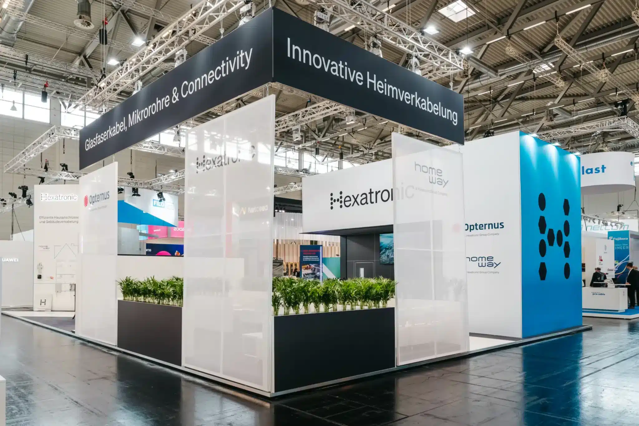 Rückseite des Hexatronic Messestandes mit großen Bannern „Glasfaserkabel, Mikrorohre & Connectivity“ sowie „Innovative Heimverkabelung“.