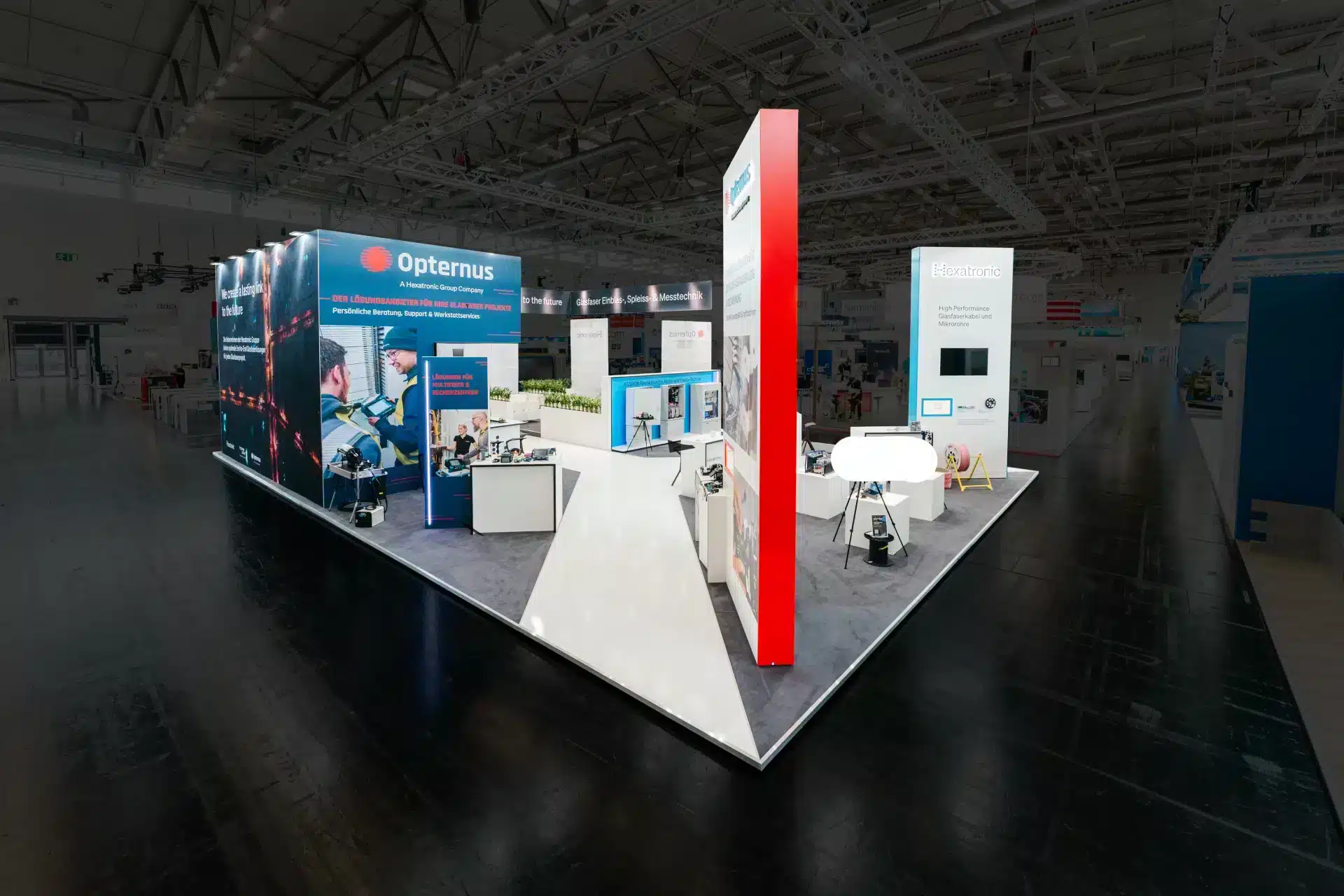 Modern gestalteter Messestand mit Opternus- und Hexatronic-Branding, Sitzgelegenheiten und Technik-Displays.