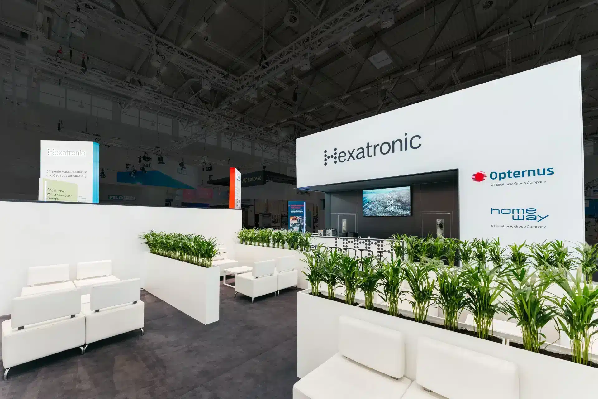 Moderner Messestand von Hexatronic und Opternus mit Lounge-Bereich und vielen grünen Pflanzen.