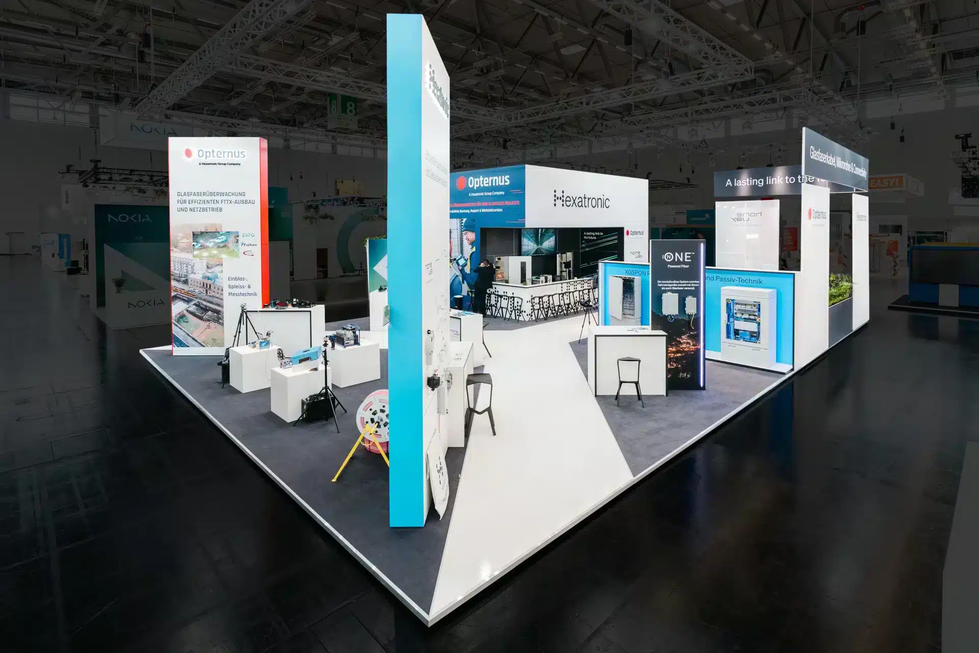 Gesamtansicht des Messestandes von Hexatronic und Opternus in Köln, mit Präsentationsflächen, Technik-Exponaten und heller Standarchitektur.