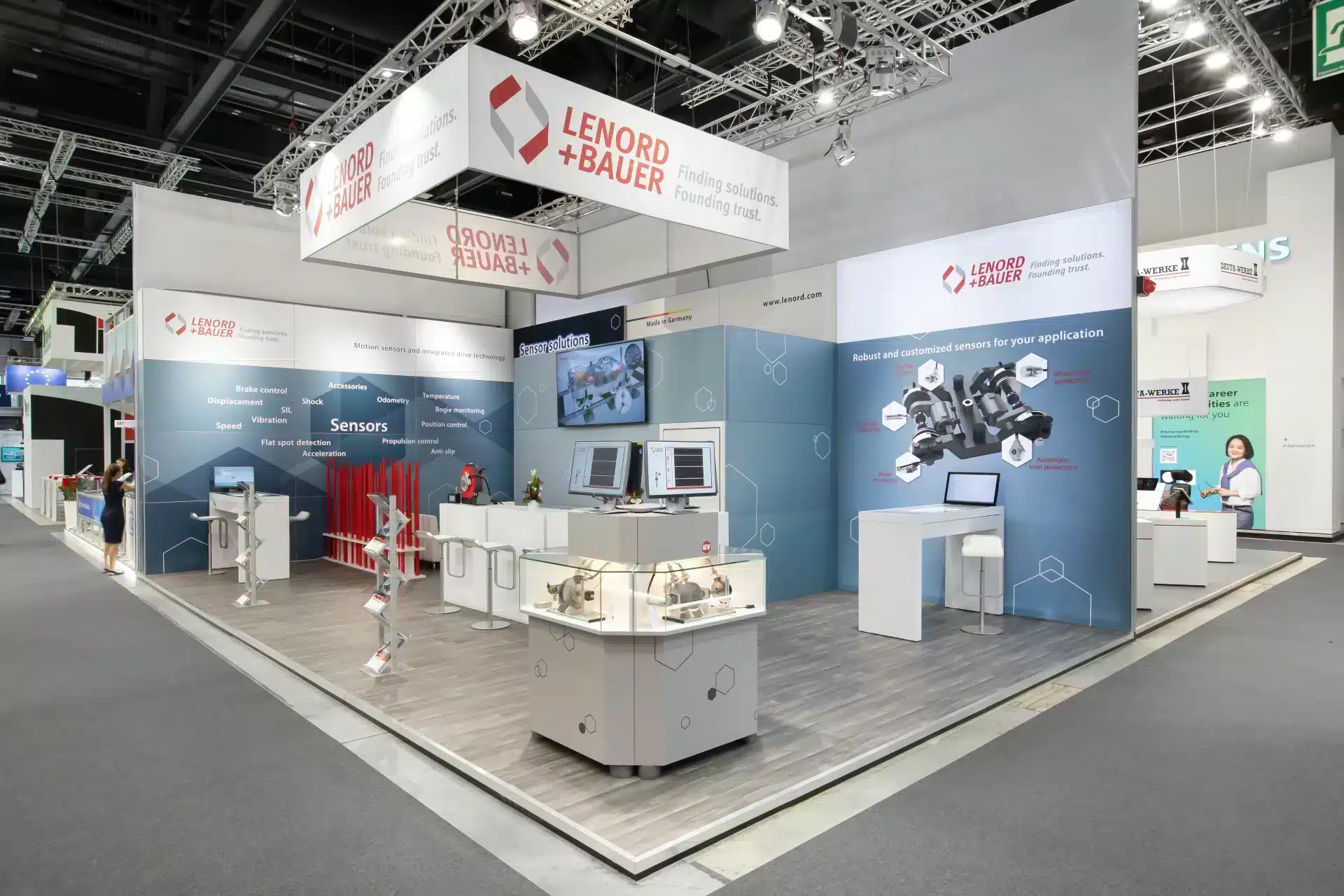 Seitenansicht des Lenord + Bauer Messestands mit modernem Boden und Vitrine mit Sensortechnik.