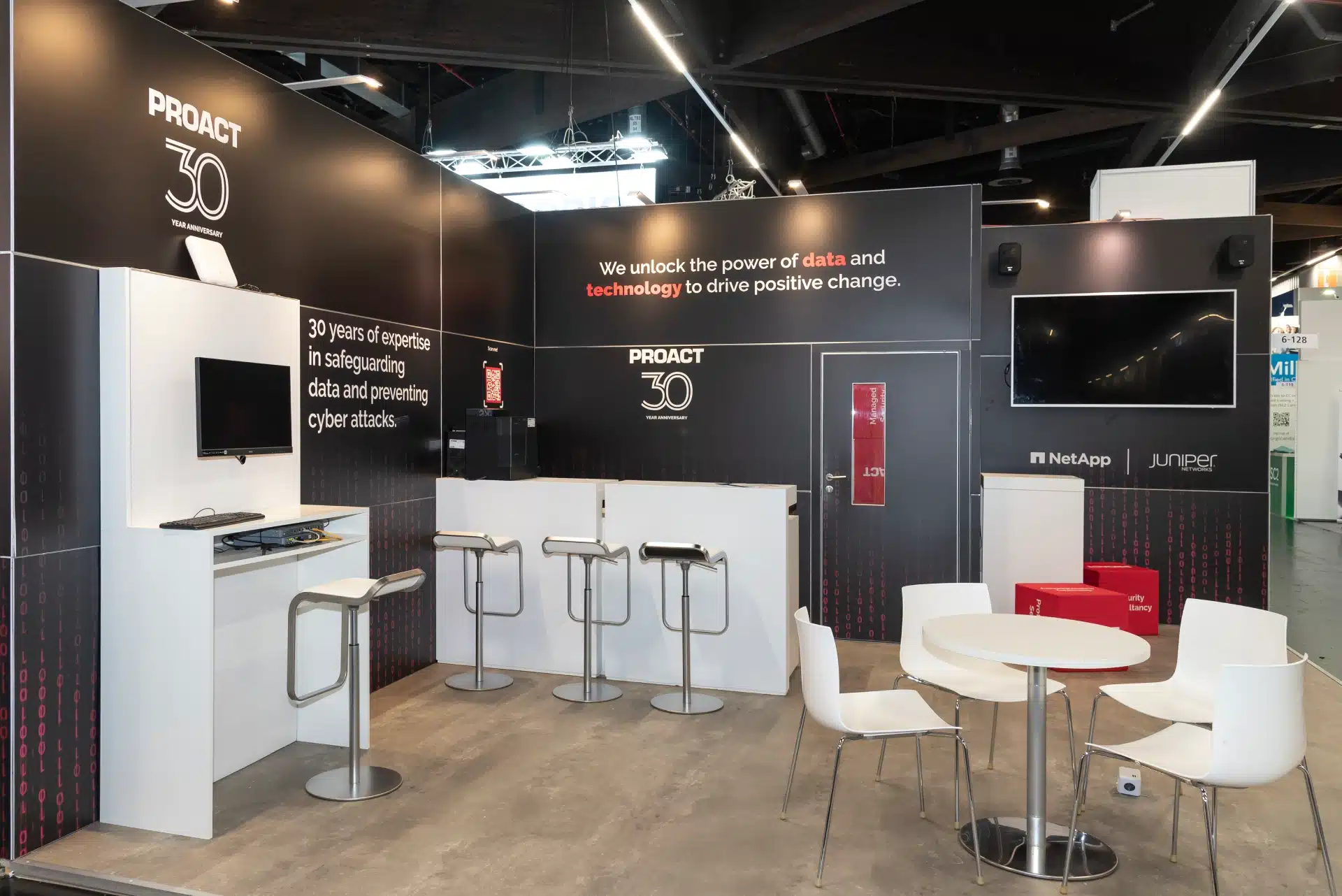 Proact Messestand auf der it-sa 2024 in Nürnberg mit modernem schwarz-weiß Design, Jubiläumslogo „30 Years Anniversary“ und Partnern NetApp und Juniper, Messebau Nürnberg.