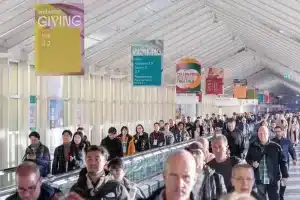 Im Korridor der Ambiente-Konferenzhalle herrscht reges Treiben. Bunte Schilder an der Decke weisen auf verschiedene Veranstaltungen und Säle wie „GIVING“ und „WORKING“ hin. Ein Glasdach erhellt den lebendigen Raum.