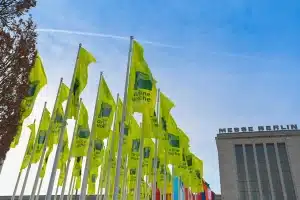 Gelbe Fahnen mit der Aufschrift „Grüne Woche“ wehen anmutig in der Nähe der Messe Berlin vor einem klaren blauen Himmel, während eine Reihe internationaler Flaggen der Szene im Hintergrund lebendige Farbe verleiht.