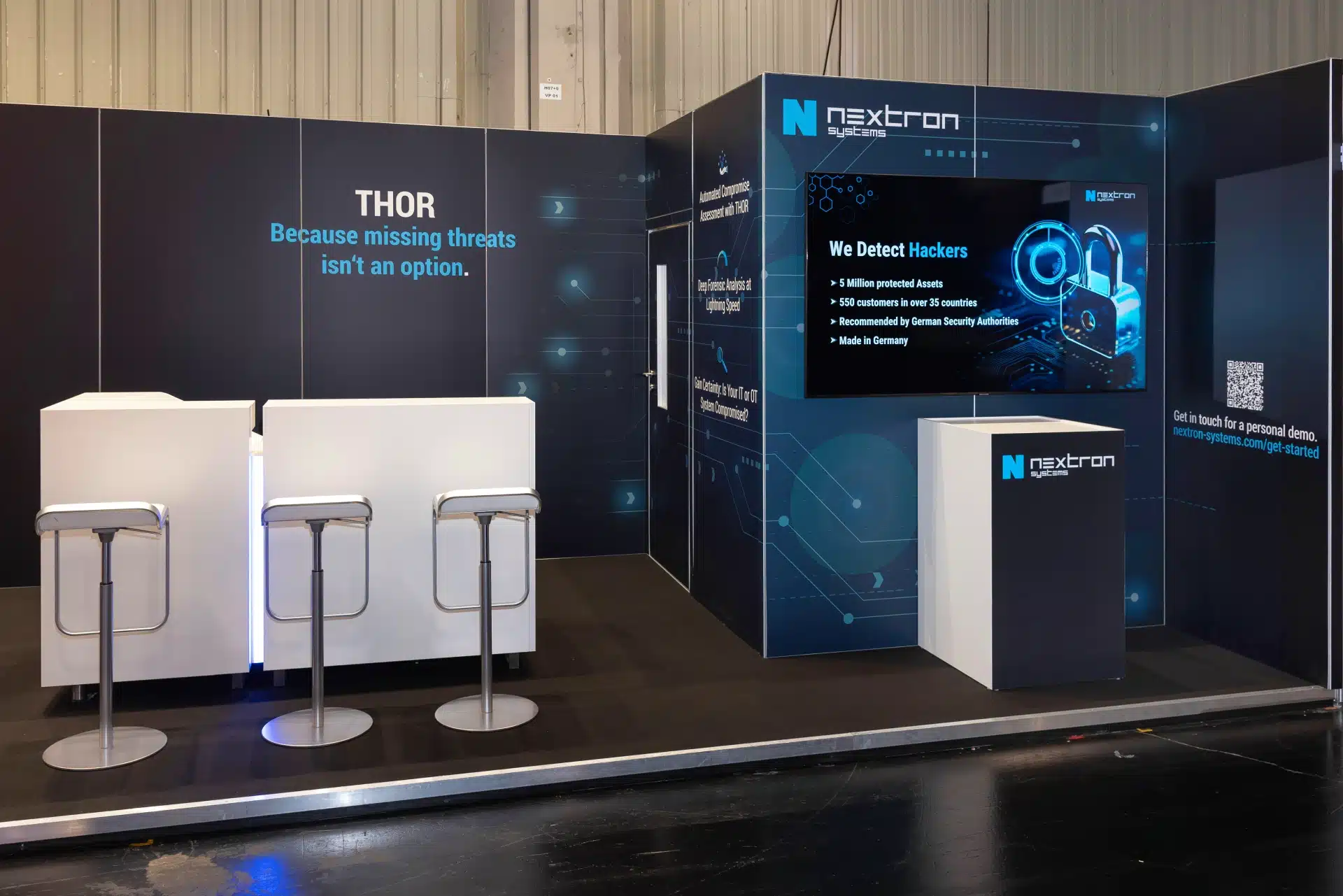 Detailansicht des Nextron Systems Messestands auf der it-sa 2024 in Nürnberg mit Theke, Barhockern und LED-Screens.