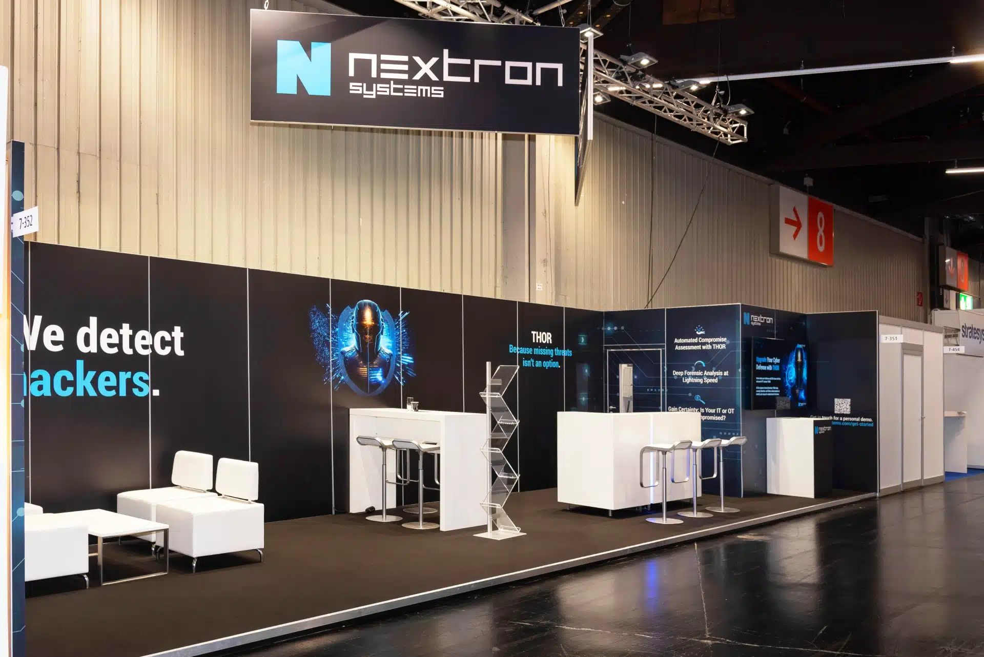 Moderner Messestand von Nextron Systems auf der it-sa 2024 in Nürnberg mit großem Deckenbanner und schwarzen Wänden im Cyber-Security-Design.