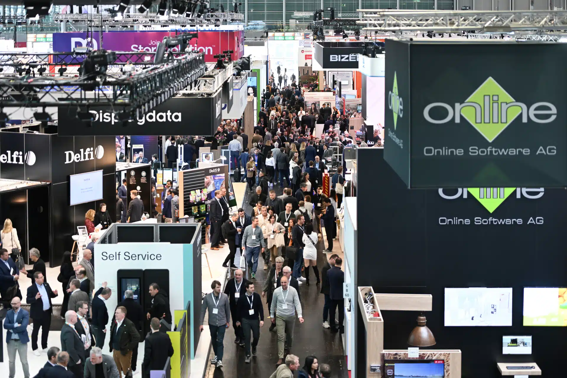 Auf der EuroShop-Messe herrscht reges Treiben mit zahlreichen Ständen und Beschilderungen, darunter auch „Online Software AG“. Besucher in Business-Kleidung unterhalten sich mit Ausstellern, während helle Beleuchtung und moderne Displays für eine lebendige Atmosphäre sorgen.