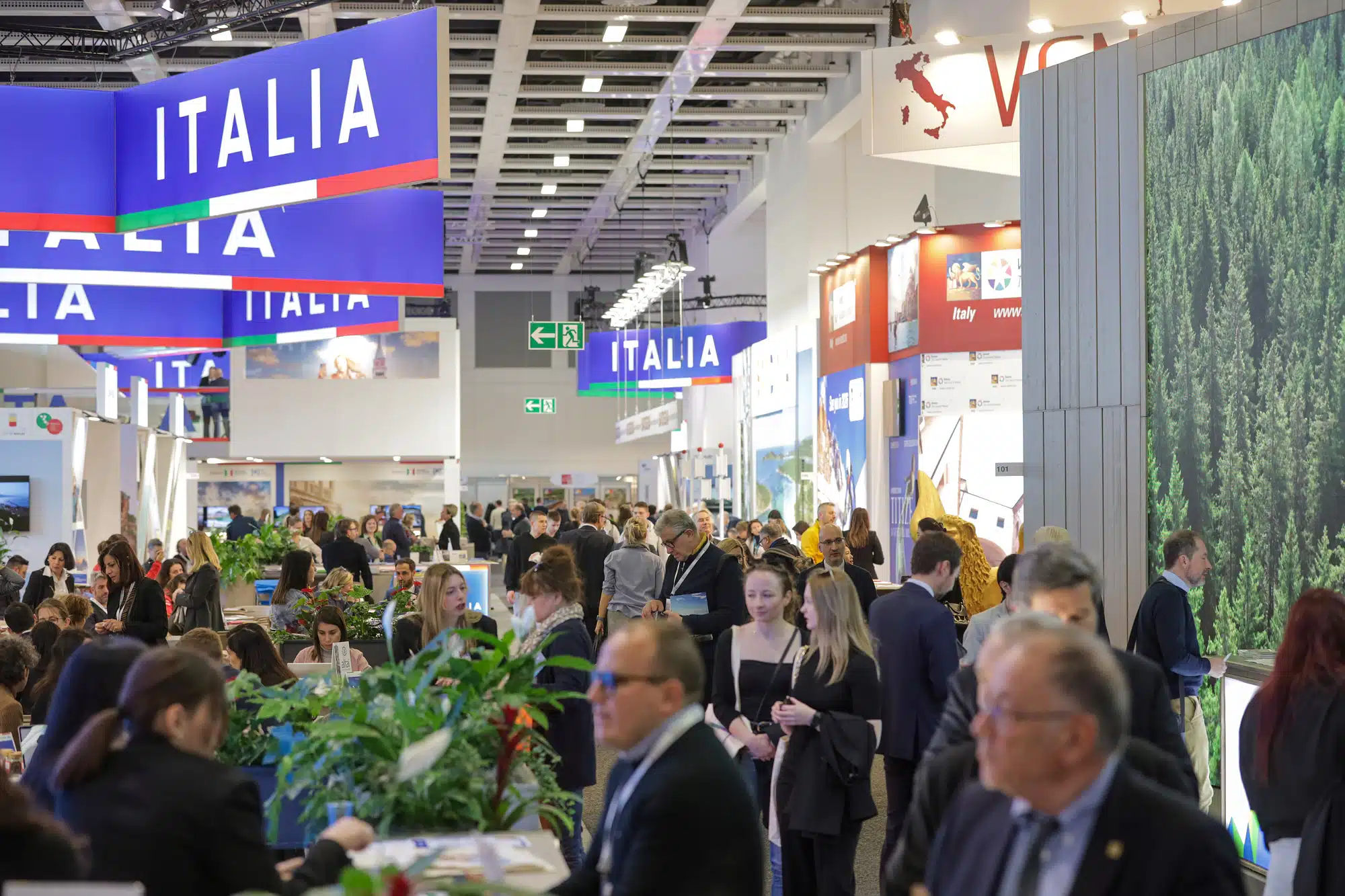 Auf der ITB Berlin herrscht reges Treiben an den bunten Messeständen. Über den Köpfen prangt stolz „ITALIA“. Die lichtdurchflutete Halle ist mit Pflanzen und digitalen Bildschirmen geschmückt und bietet ein buntes Publikum.