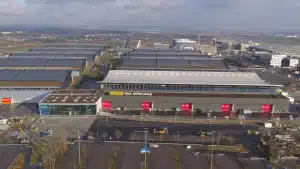 Das große Kongresszentrum Paul Horn Halle, umgeben von Parkplätzen und Industriegebäuden, ist Schauplatz des dynamischen Stuttgarter MesseHerbst. Kräne deuten auf laufende Bauarbeiten hin, im Hintergrund sind sanfte Hügel und ein bewölkter Himmel zu sehen.