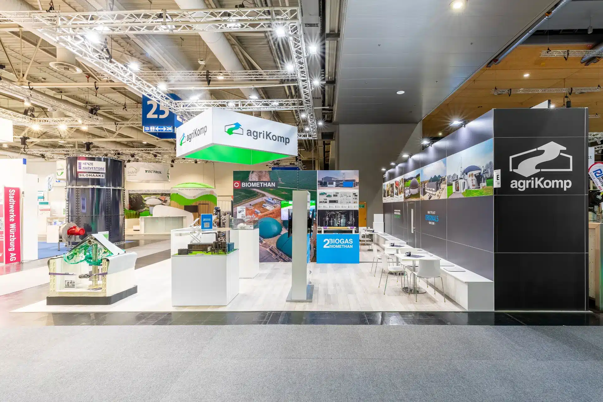 Messestand mit „agriKomp“-Logo und Präsentationen zur Biogastechnologie. Der Stand ist modern gestaltet und verfügt über LED-Bildschirme, Informationsplakate sowie Sitzbereiche mit Tischen und Stühlen. Deckenbeleuchtung hebt verschiedene Produkte und Schilder hervor.