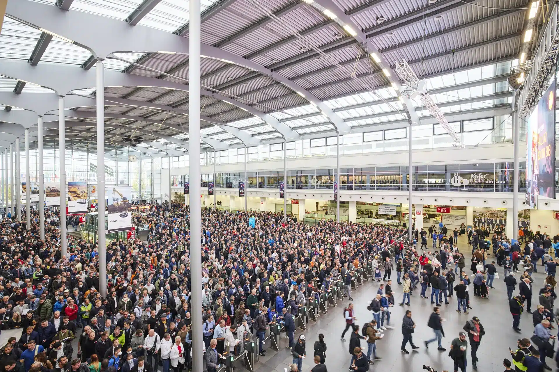 Eine große Menschenmenge füllt das geräumige Kongresszentrum, das mit seinen hohen Decken und Glasfronten an die bauma erinnert. Besucher reihen sich in der Nähe von Ständen und Ausstellungen auf. Die helle Beleuchtung und die geschäftige Atmosphäre lassen eine dynamische Ausstellung erwarten.