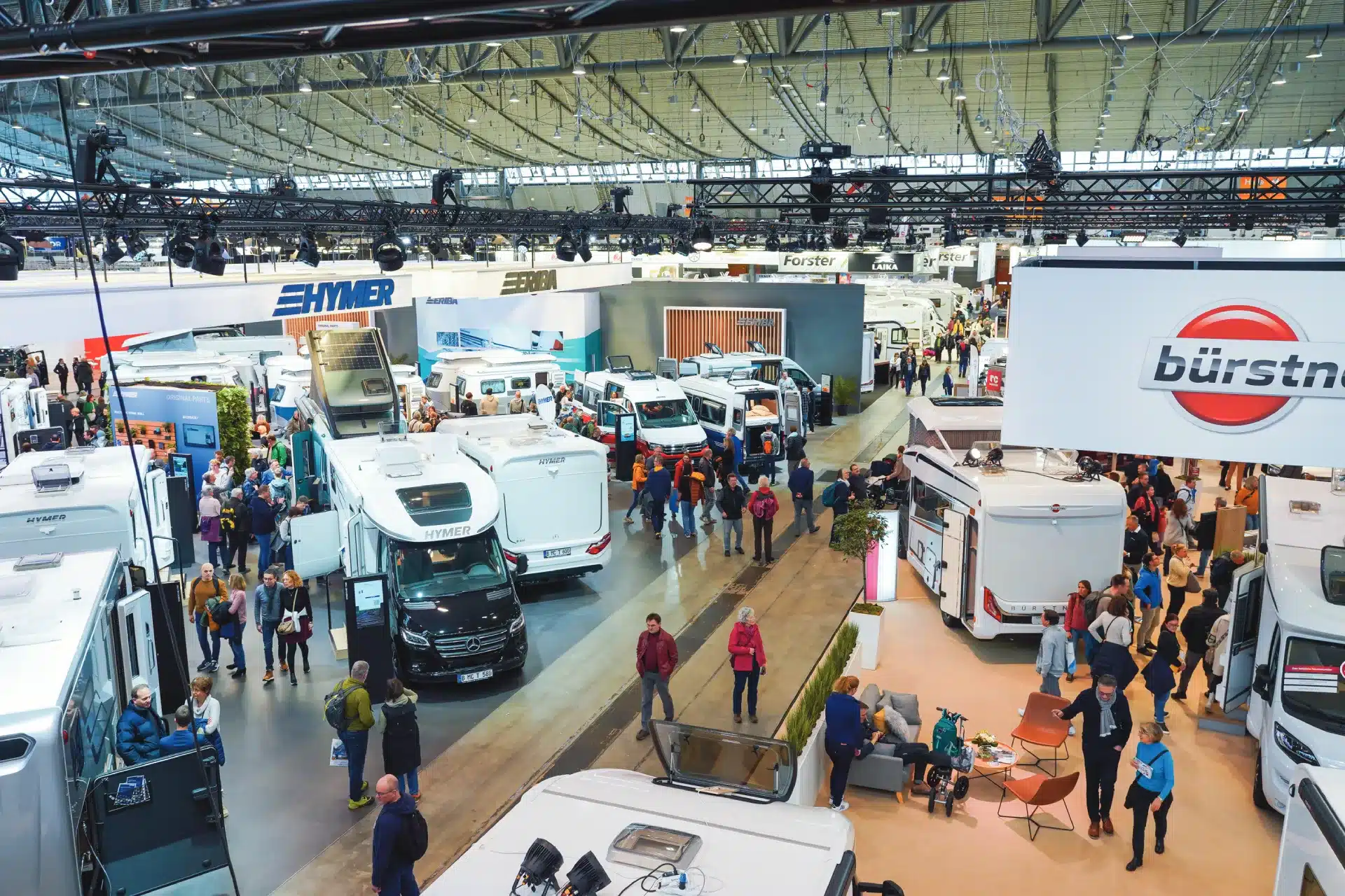 Eine geschäftige Messehalle voller Wohnmobile und Campervans – auf der CMT herrscht reges Treiben. Zahlreiche Besucher entdecken die Fahrzeuge, während Stände und Markenschilder von Hymer und Bürstner ins Auge fallen. Das Ambiente ist lebendig und der großzügige, lichtdurchflutete Innenraum besticht durch sein großzügiges Ambiente.