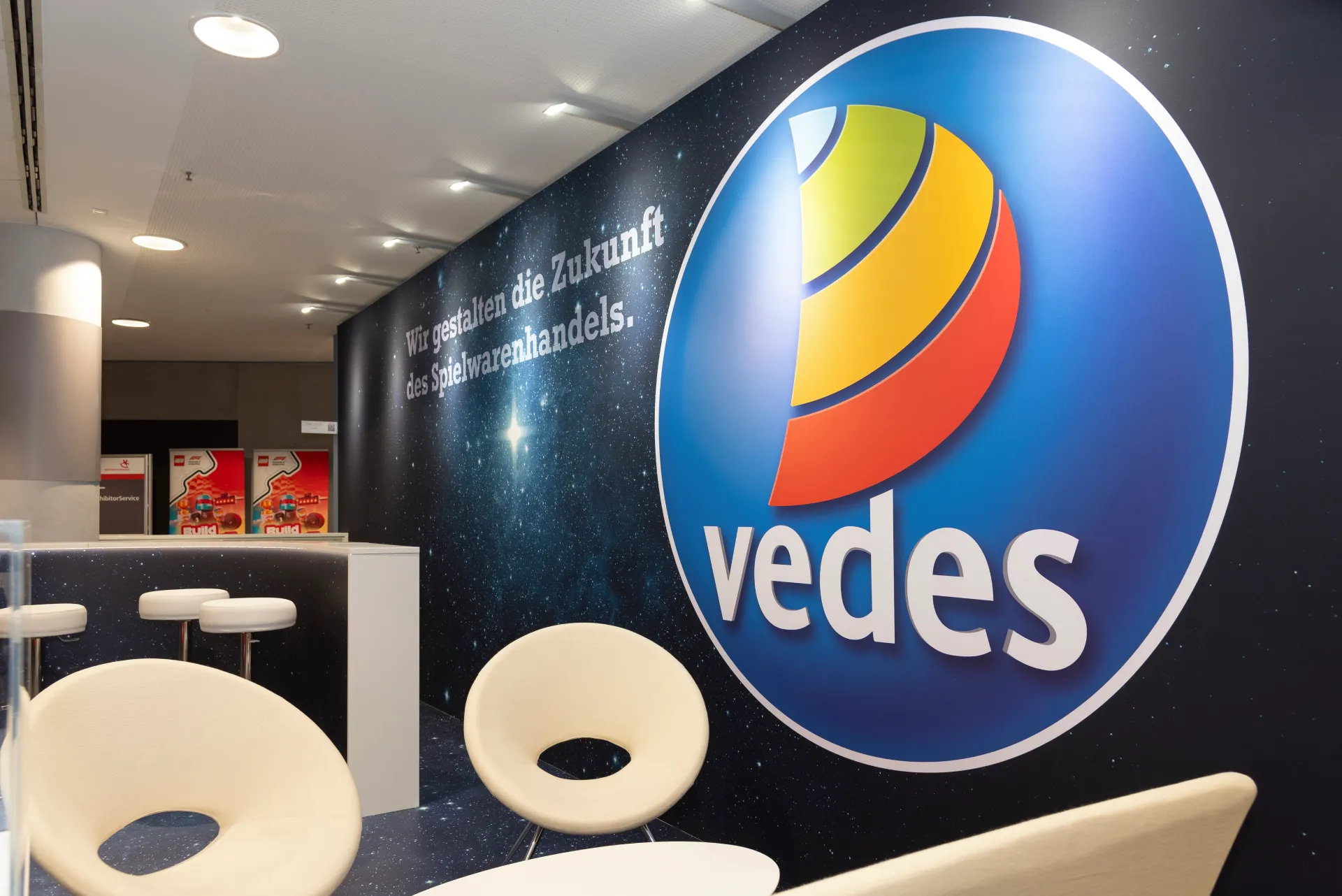 Messebau Nürnberg – Vedes Lounge-Bereich mit großem Firmenlogo und Slogan auf der Spielwarenmesse 2025 in Nürnberg.