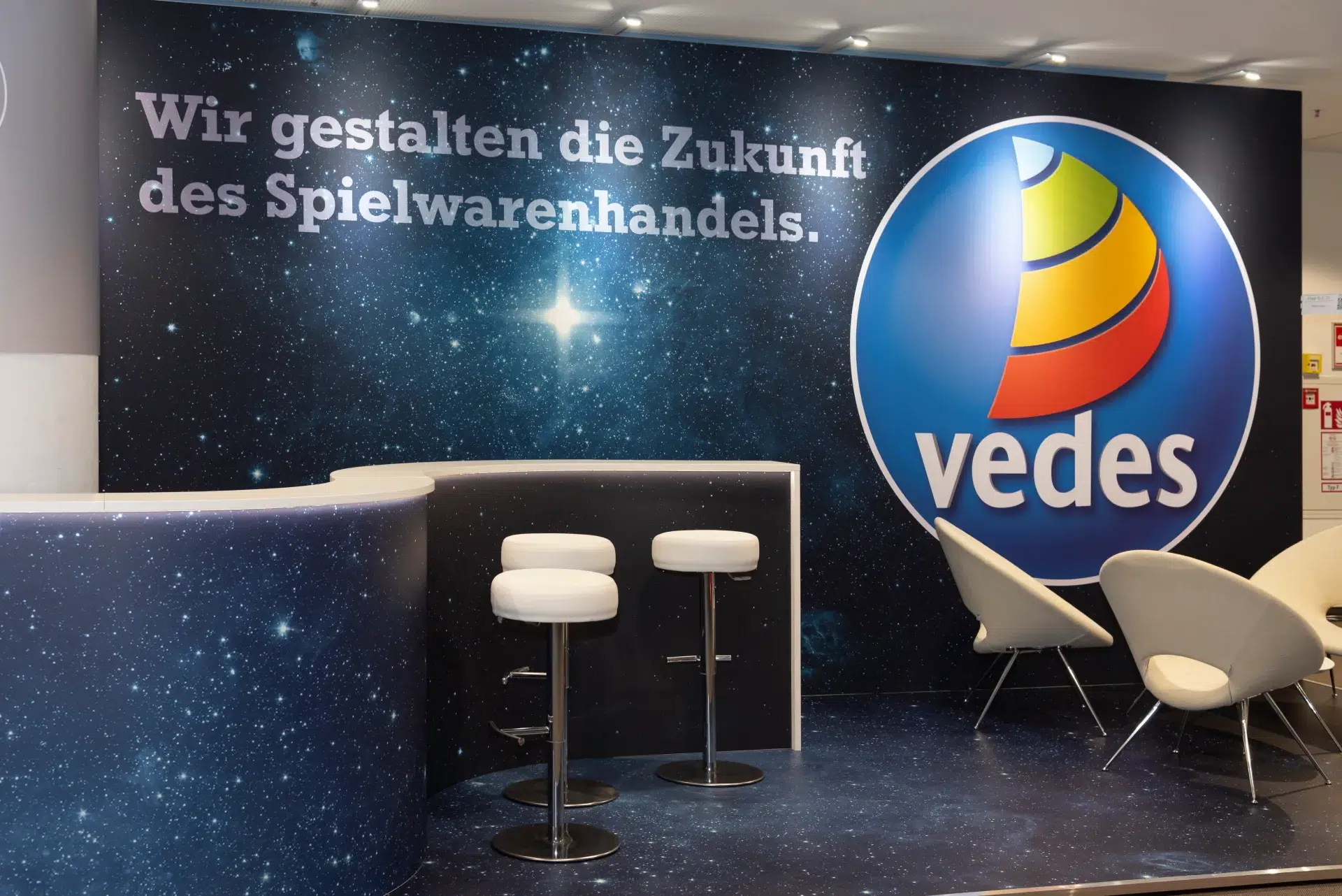 Messebau Nürnberg – Empfangsbereich des Vedes Messestands mit Barhockern und Firmenlogo im Sternendesign auf der Spielwarenmesse 2025.