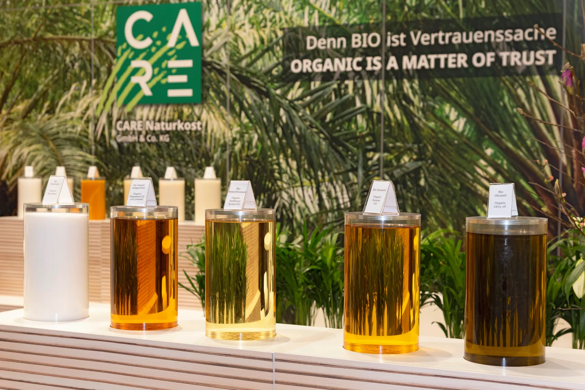 Präsentation organischer Öle in Glaszylindern am Messestand von CARE Naturkost auf der Biofach Messe 2025 in Nürnberg – Messebau Nürnberg.