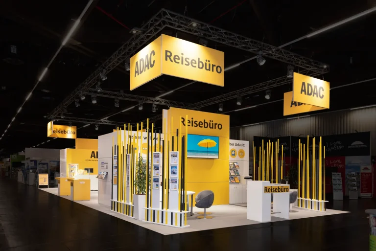 Messebau Nürnberg – ADAC Reisebüro Messestand mit gelben Hängewürfeln, Prospektwänden und Beratungslounges auf der Freizeit Touristik & Garten 2025 in Nürnberg.