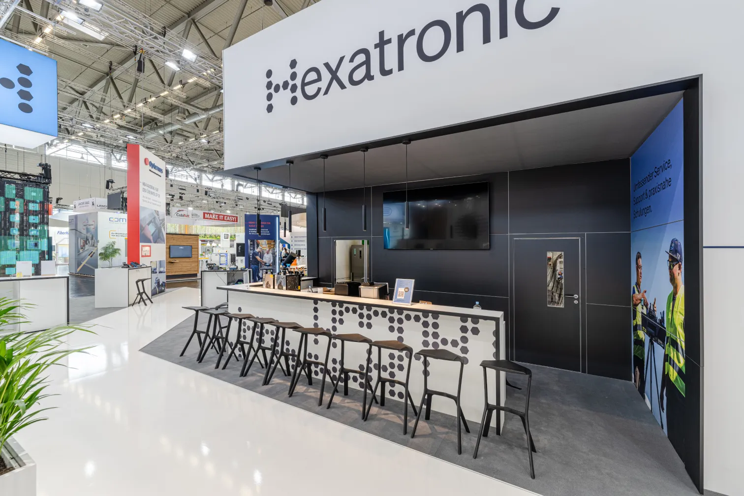 Messebau Köln – moderner Messestand von Hexatronic mit Barbereich, schwarzen Hockern und klarer Markenpräsentation auf einer Messe in Köln.
